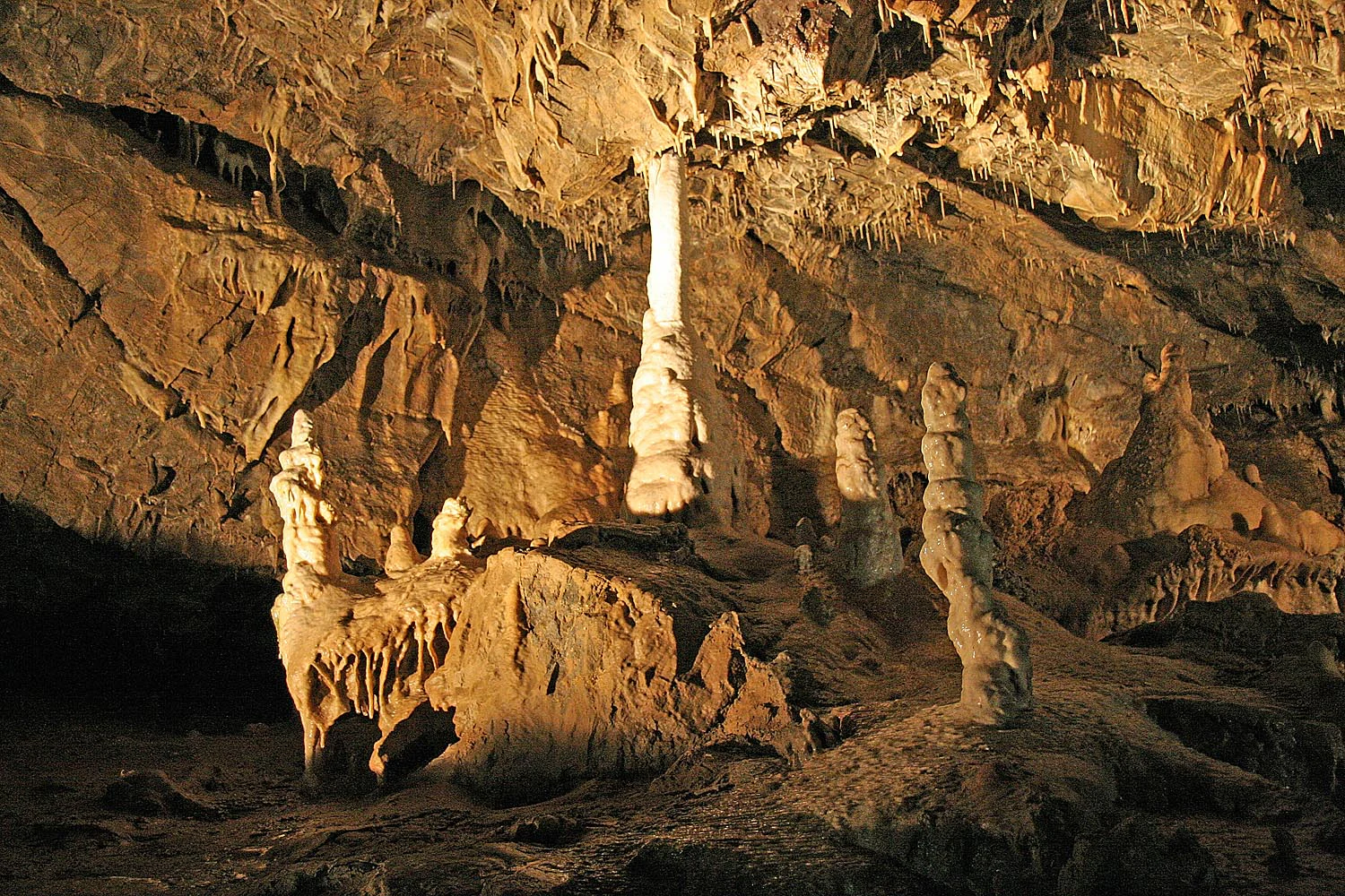 Interior of a cave with tall stalagmites and rocky formations illuminated by artificial lighting
