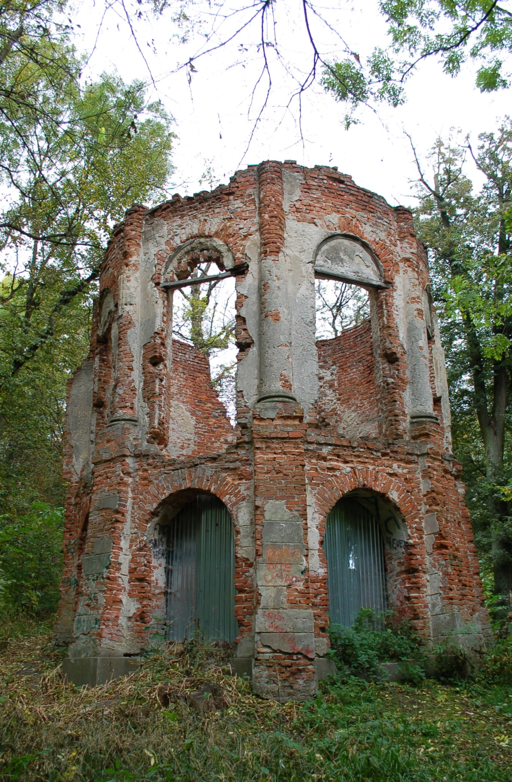 A crumbling, two-story circular brick structure, likely an old rotunda, sits in the middle of a forest clearing in Morysin Nature Reserve.