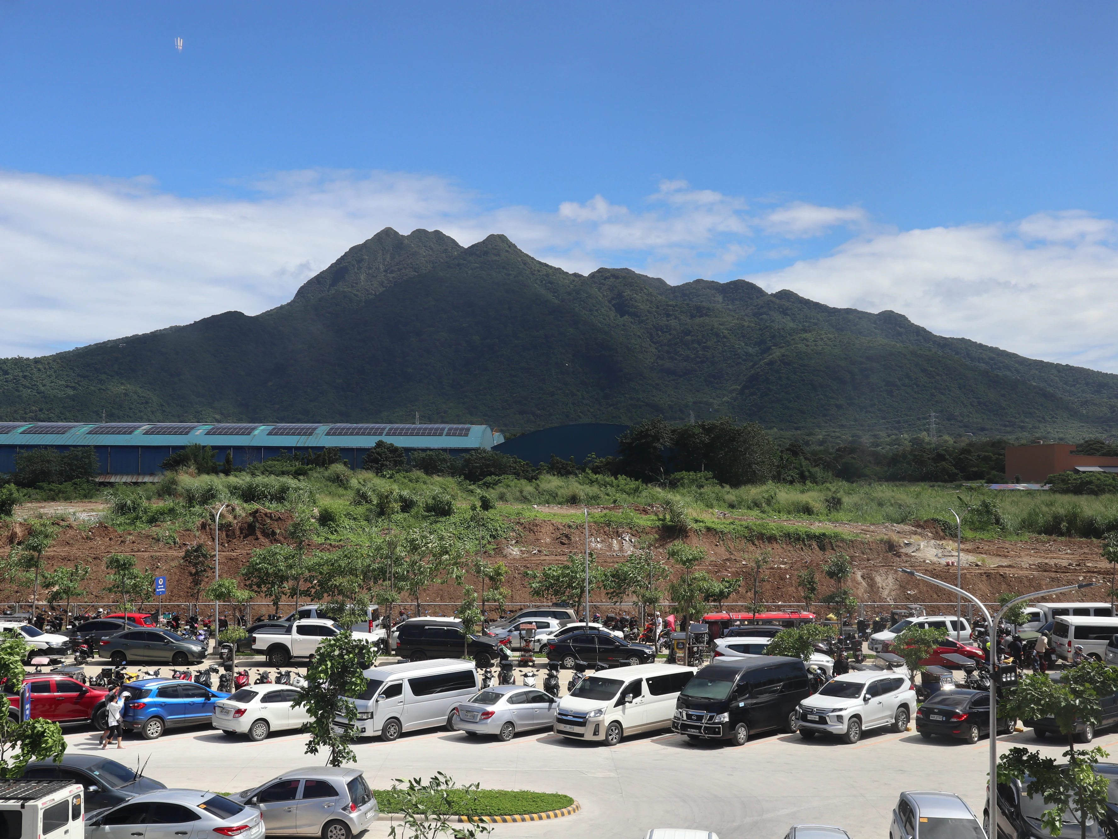 A wide view of the forested peak of Mount Makiling rising above a large, busy parking lot filled with various vehicles.