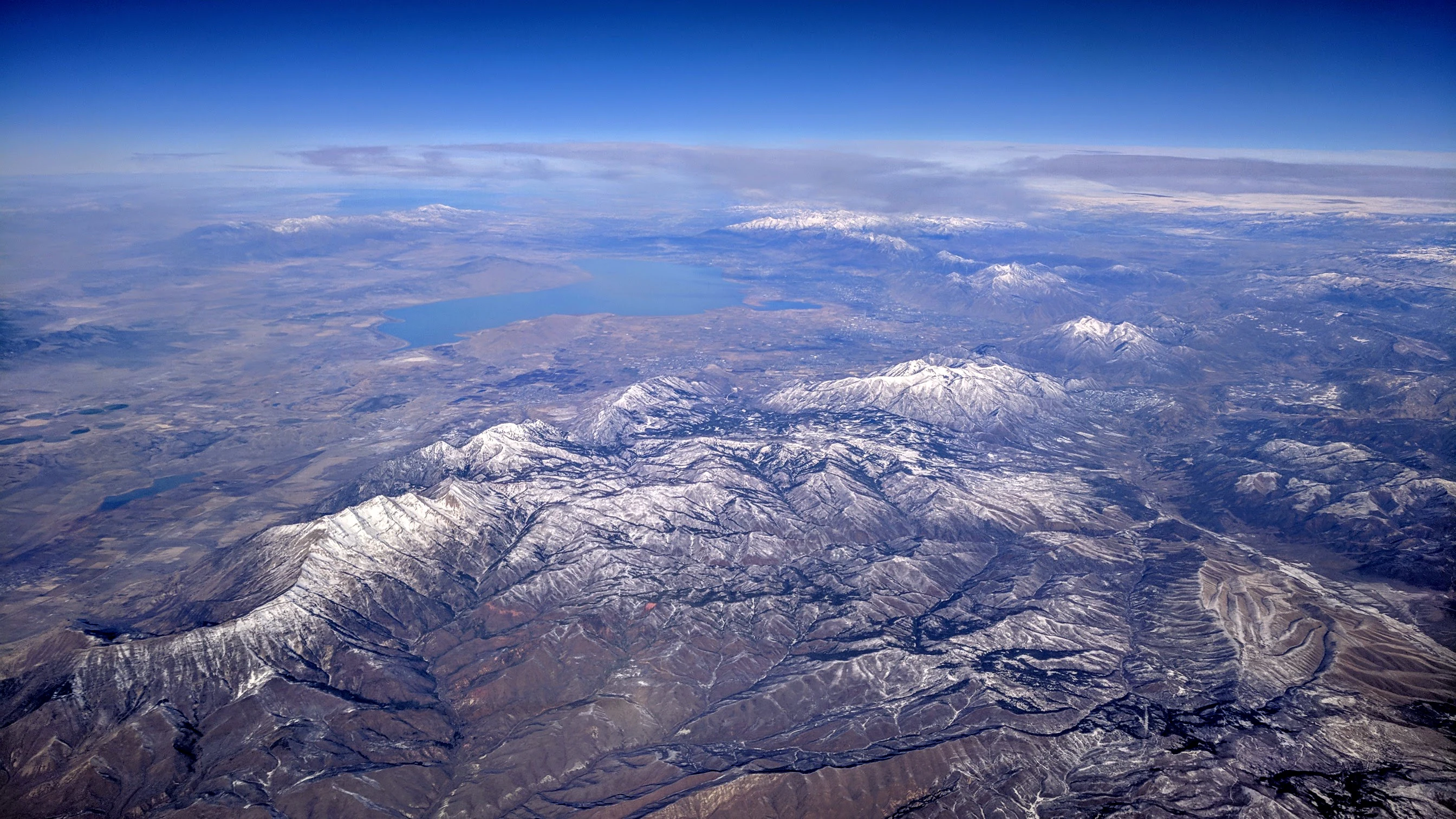 A wide aerial view of snowy mountain peaks, specifically Mount Nebo, with a large lake reflecting the sky in the background.