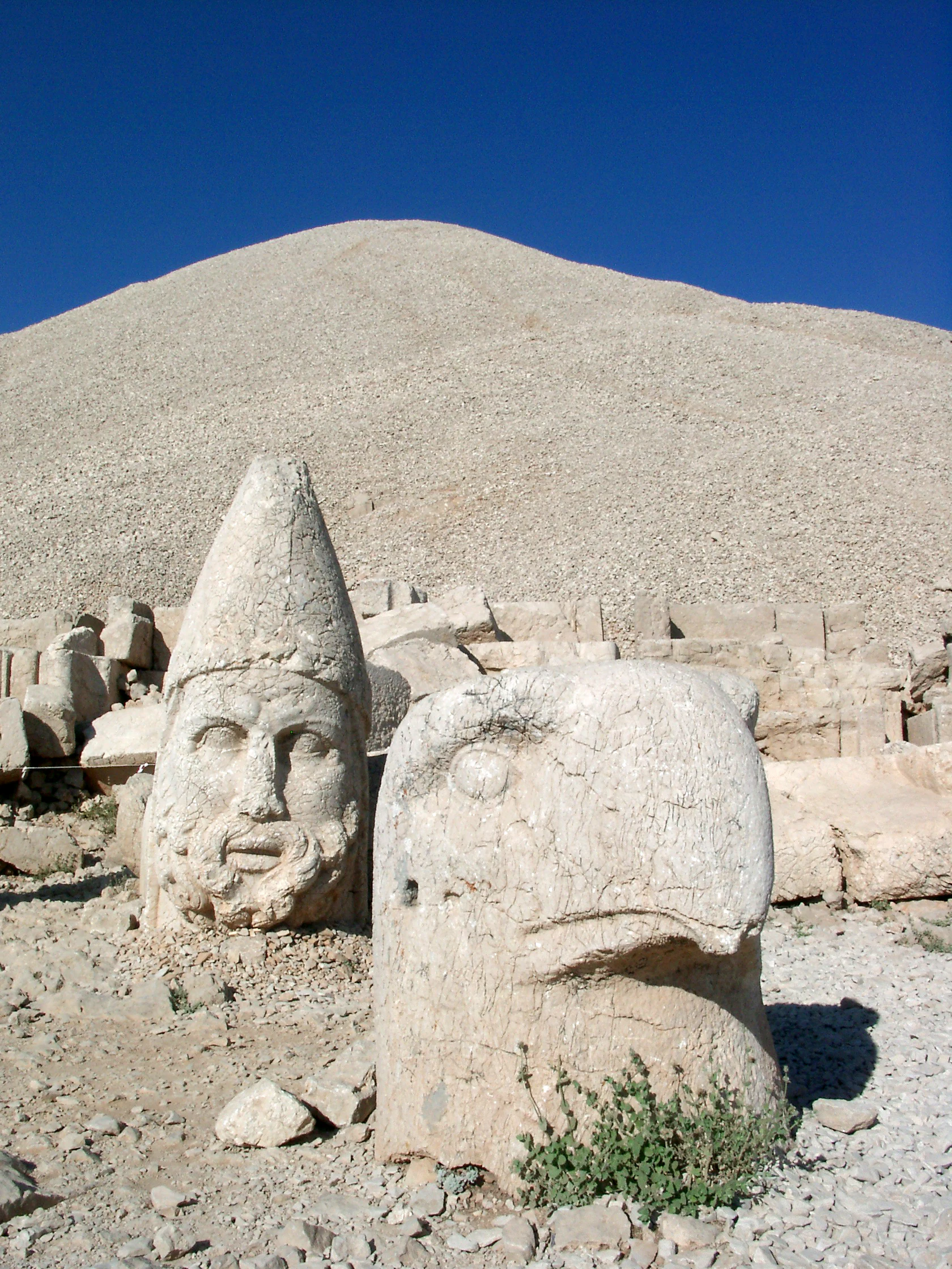 Large ancient stone statue heads in foreground with rocky hill in background