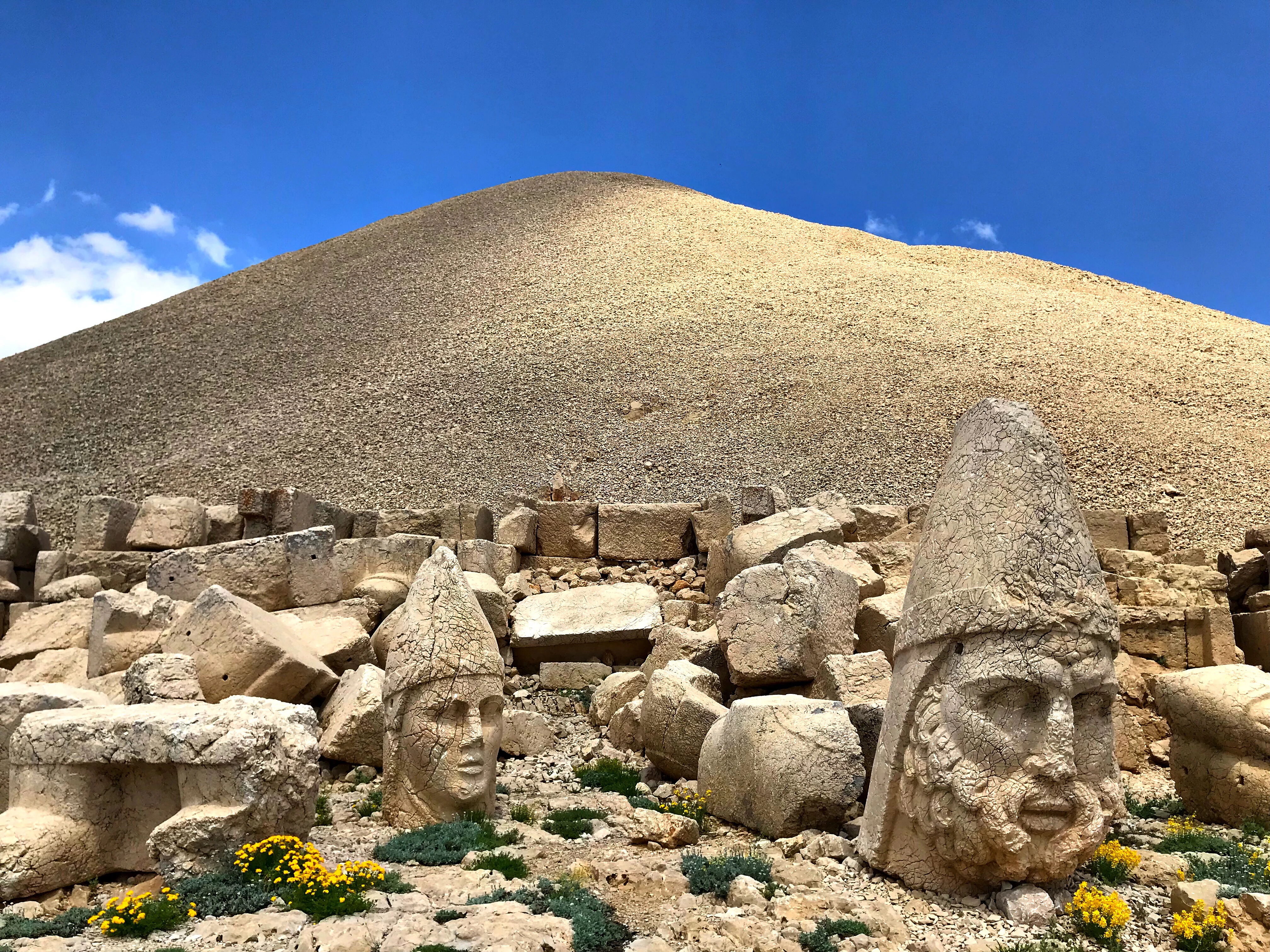 Stone heads from ancient ruins scattered on rocky terrain with Mount Nemrut mound in background under clear blue sky