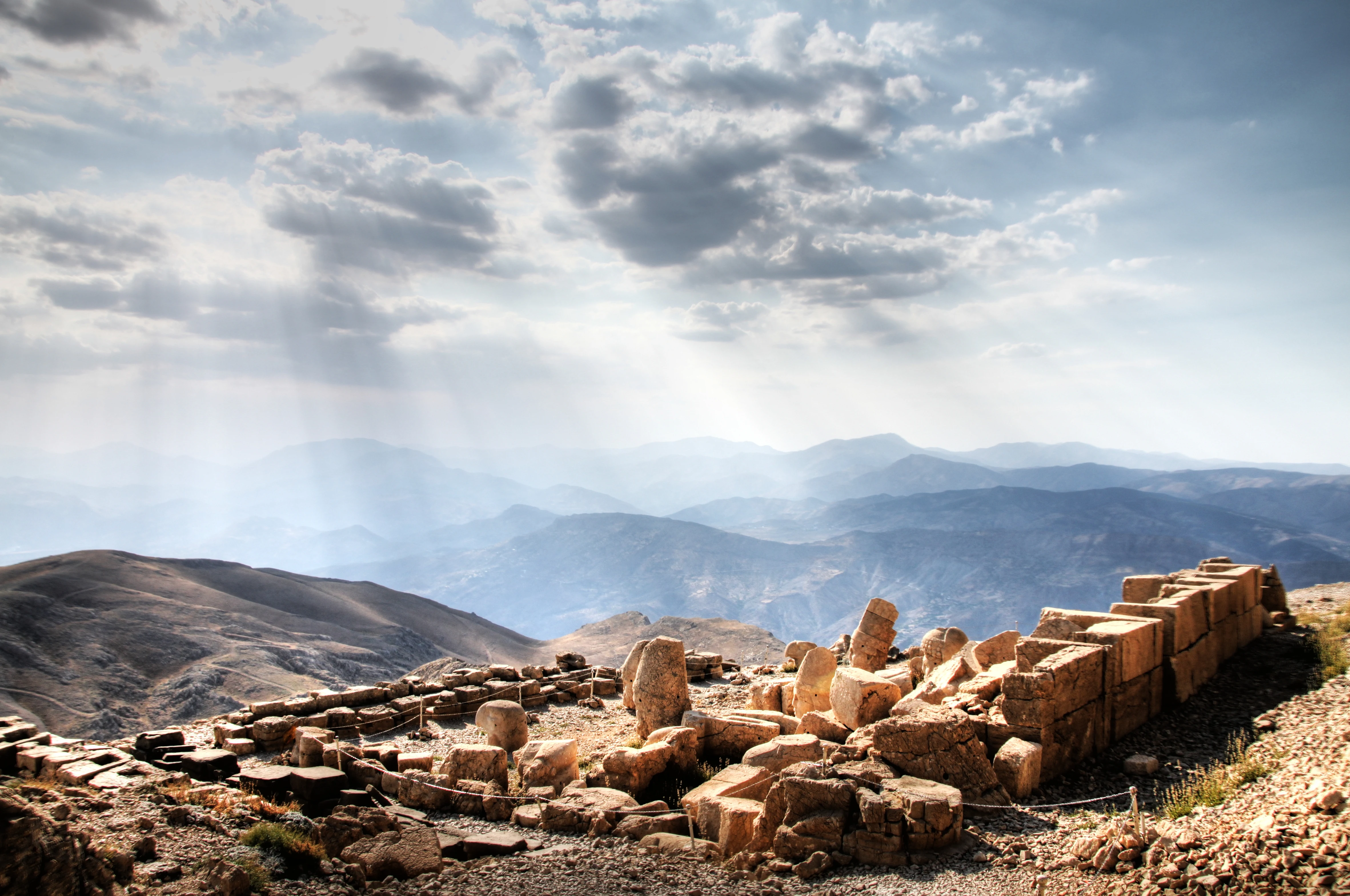Ancient stone ruins on a mountain peak with distant mountains and partly cloudy sky