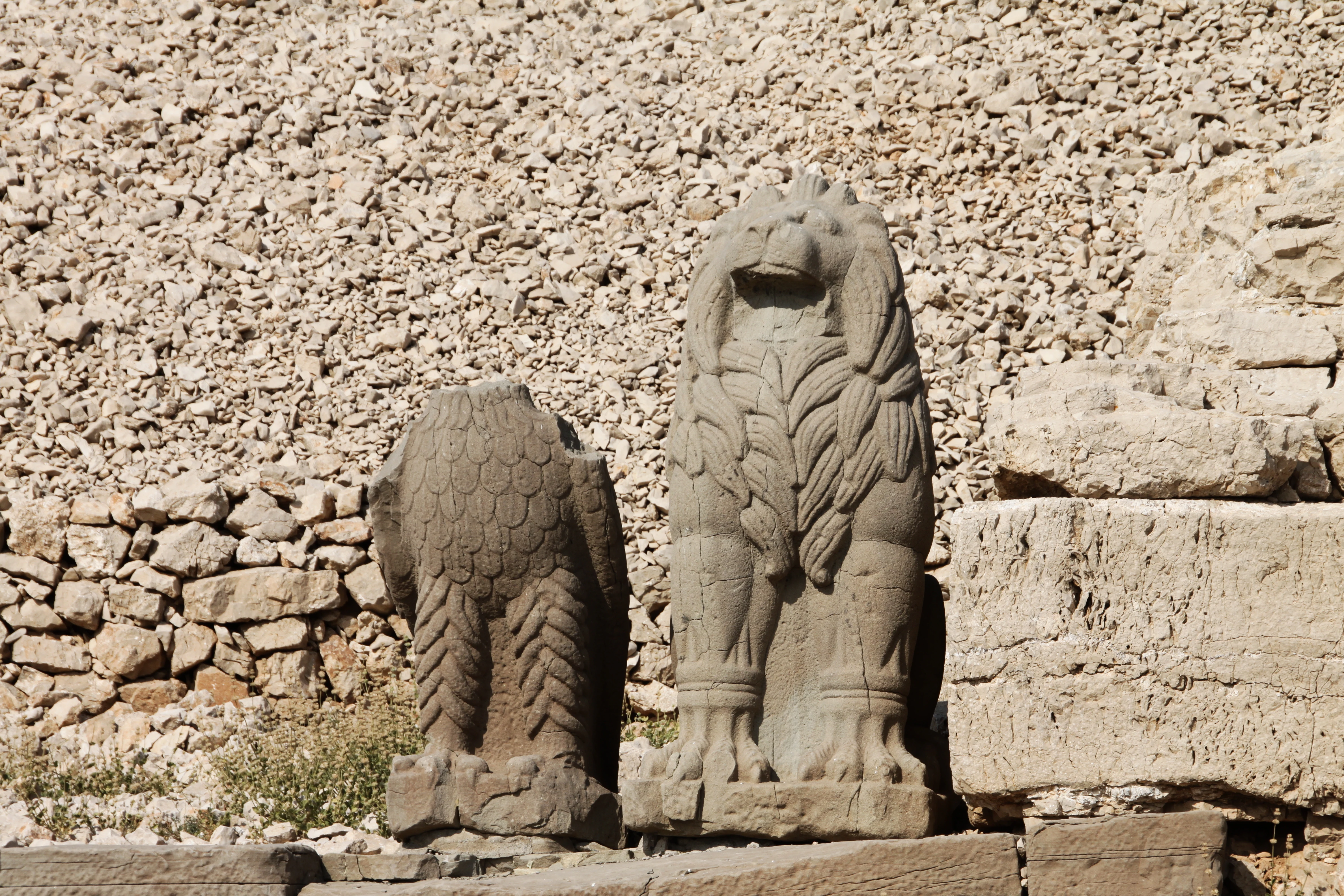 Two ancient stone statues, one of an eagle and one of a lion, standing on stone bases against a stone wall background