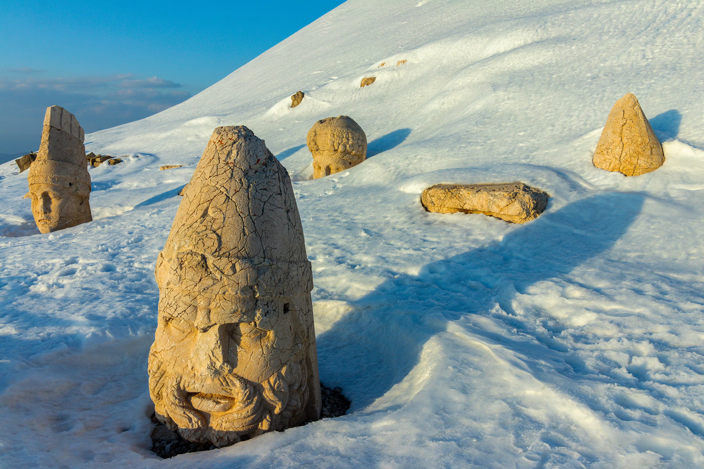 Stone statue head and ancient stone structures on snow-covered mountain slope