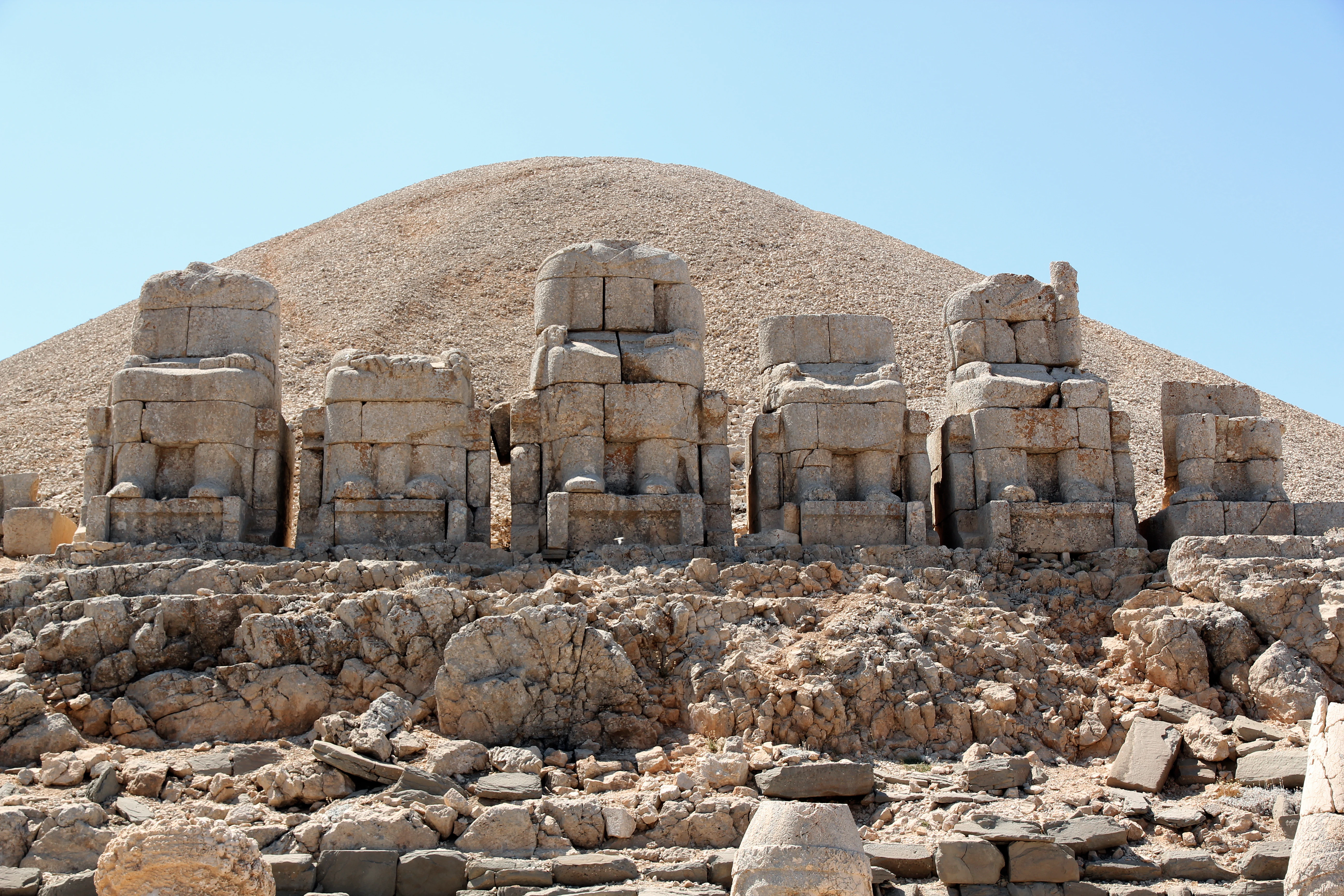Stone statues on rocky terrain with a large mound in the background under a clear sky