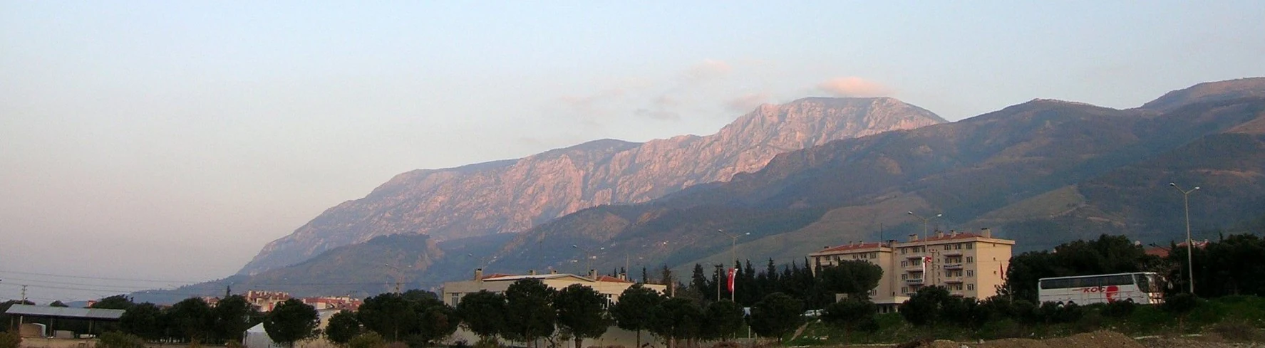 Panoramic landscape showing Mount Sipylus with a town and trees in the foreground under a clear sky
