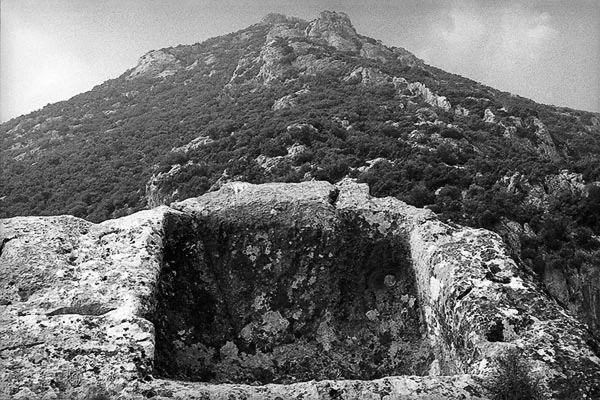 Black and white photograph of an ancient stone structure with a mountainous landscape in the background