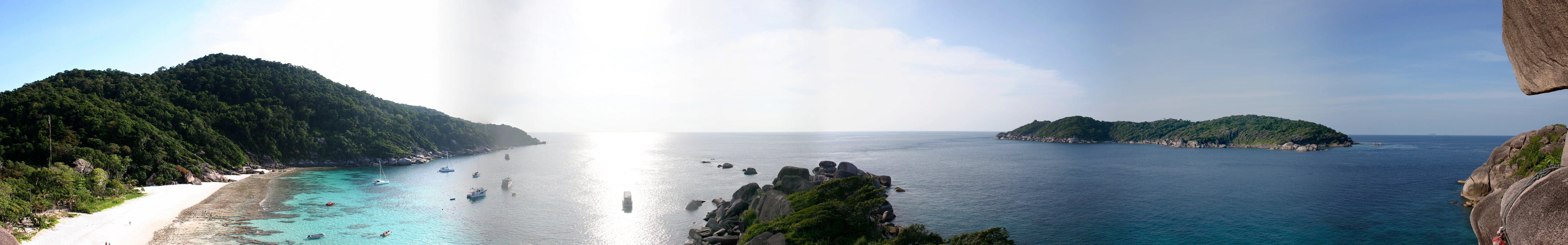 Panoramic landscape of Similan Islands showing coastal waters, sandy beach, and lush green hills with small boats in the sea