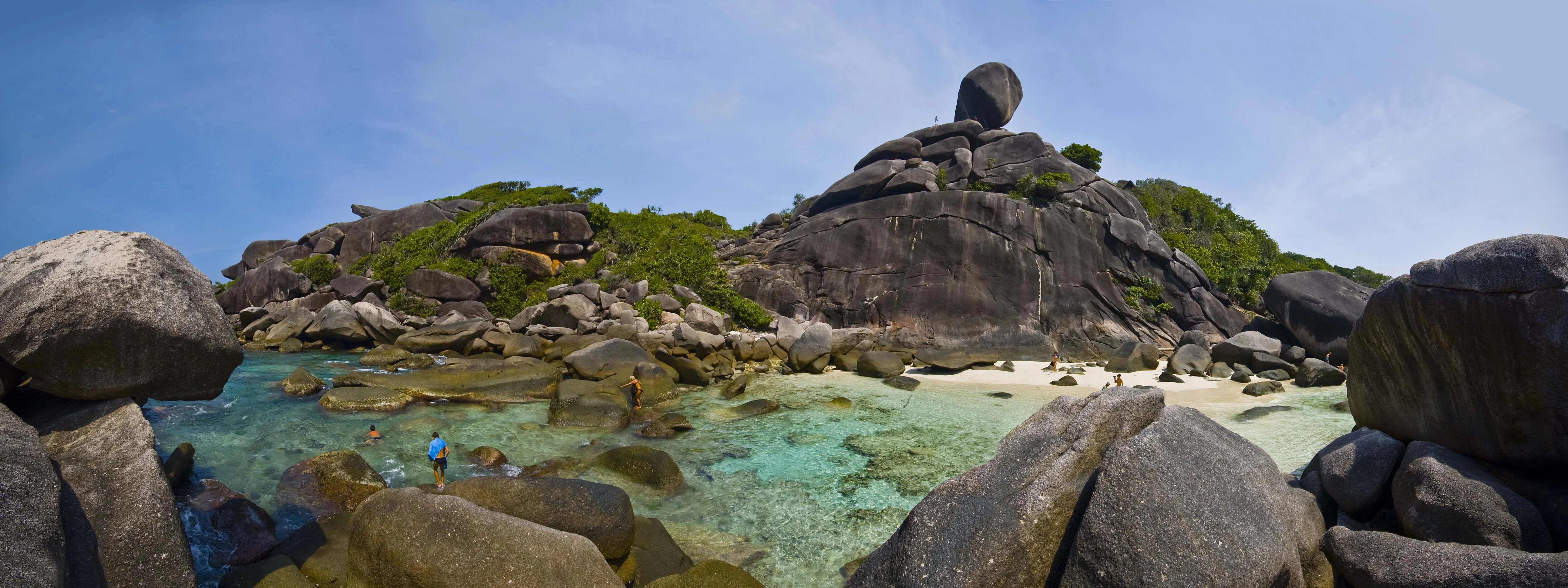 Panoramic view of Mu Ko Similan National Park showing sandy beach, turquoise waters, large granite boulders, and visitors swimming under clear blue sky