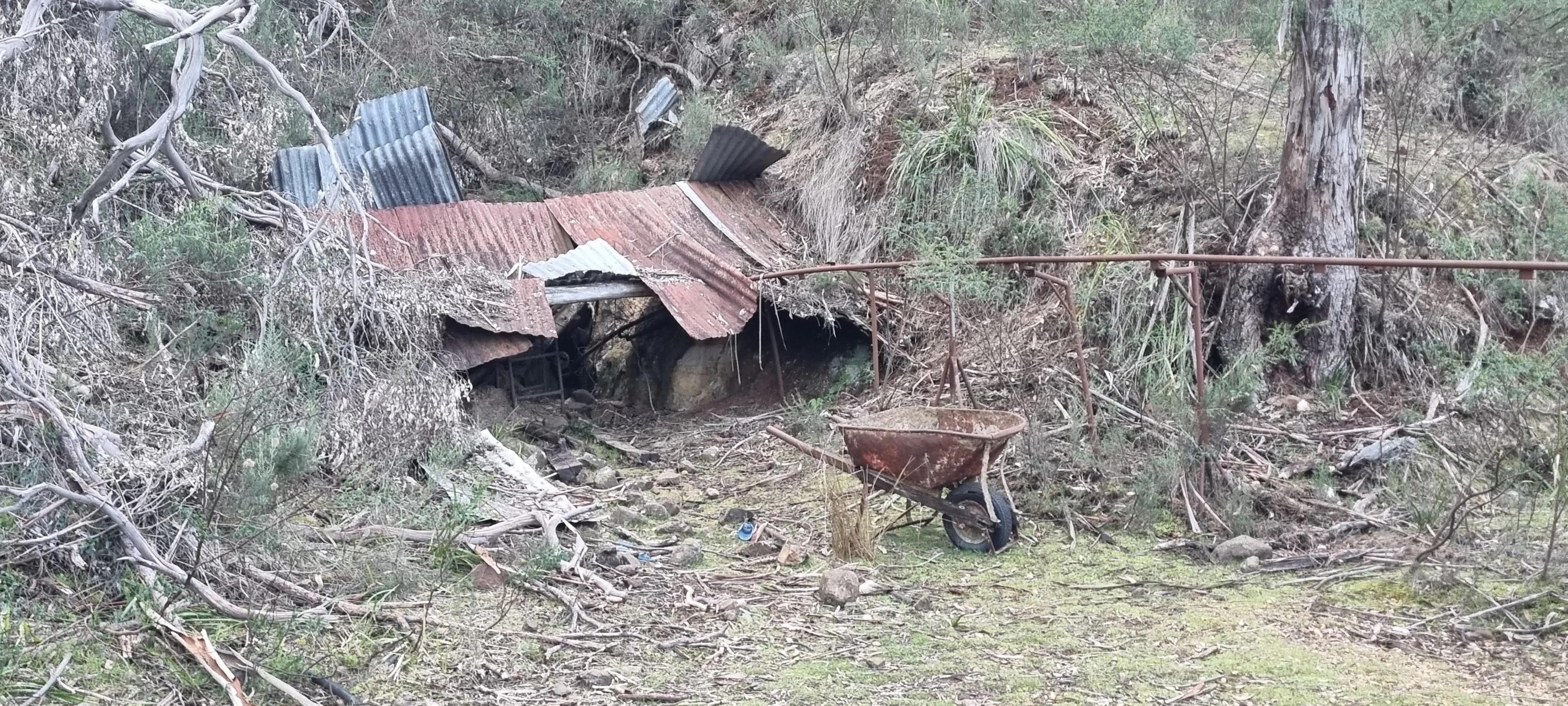 Abandoned corrugated metal shed and a rusty wheelbarrow sitting in a forest clearing, evidence of historic oil shale mining.