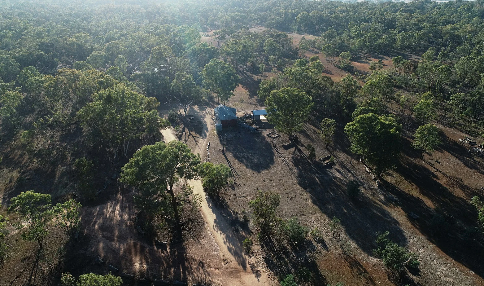 Aerial drone shot looking down onto a small wooden building in a clearing surrounded by Australian woodland.