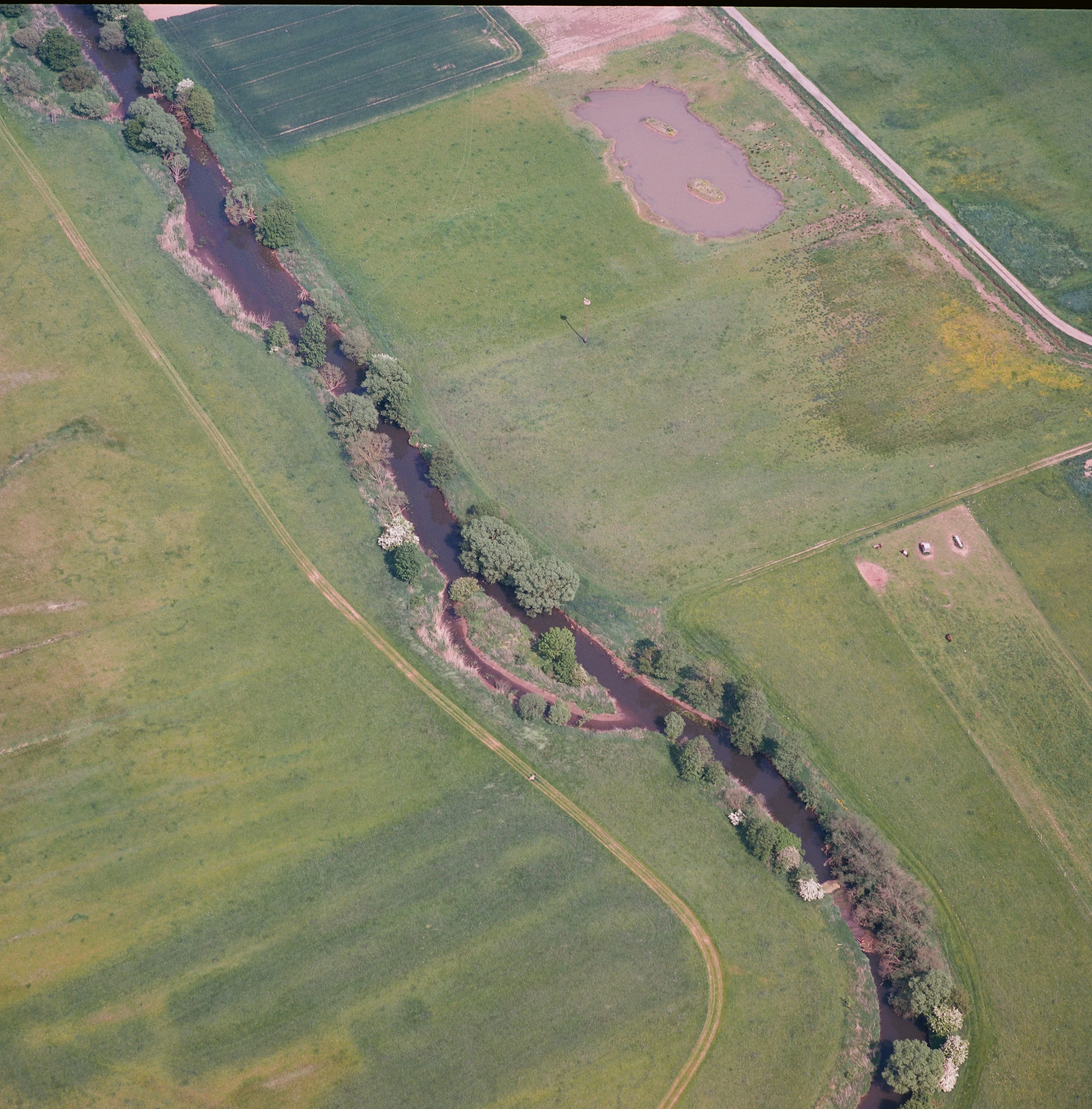 Aerial view looking down at a winding river flowing through green grasslands and fields in a nature reserve.