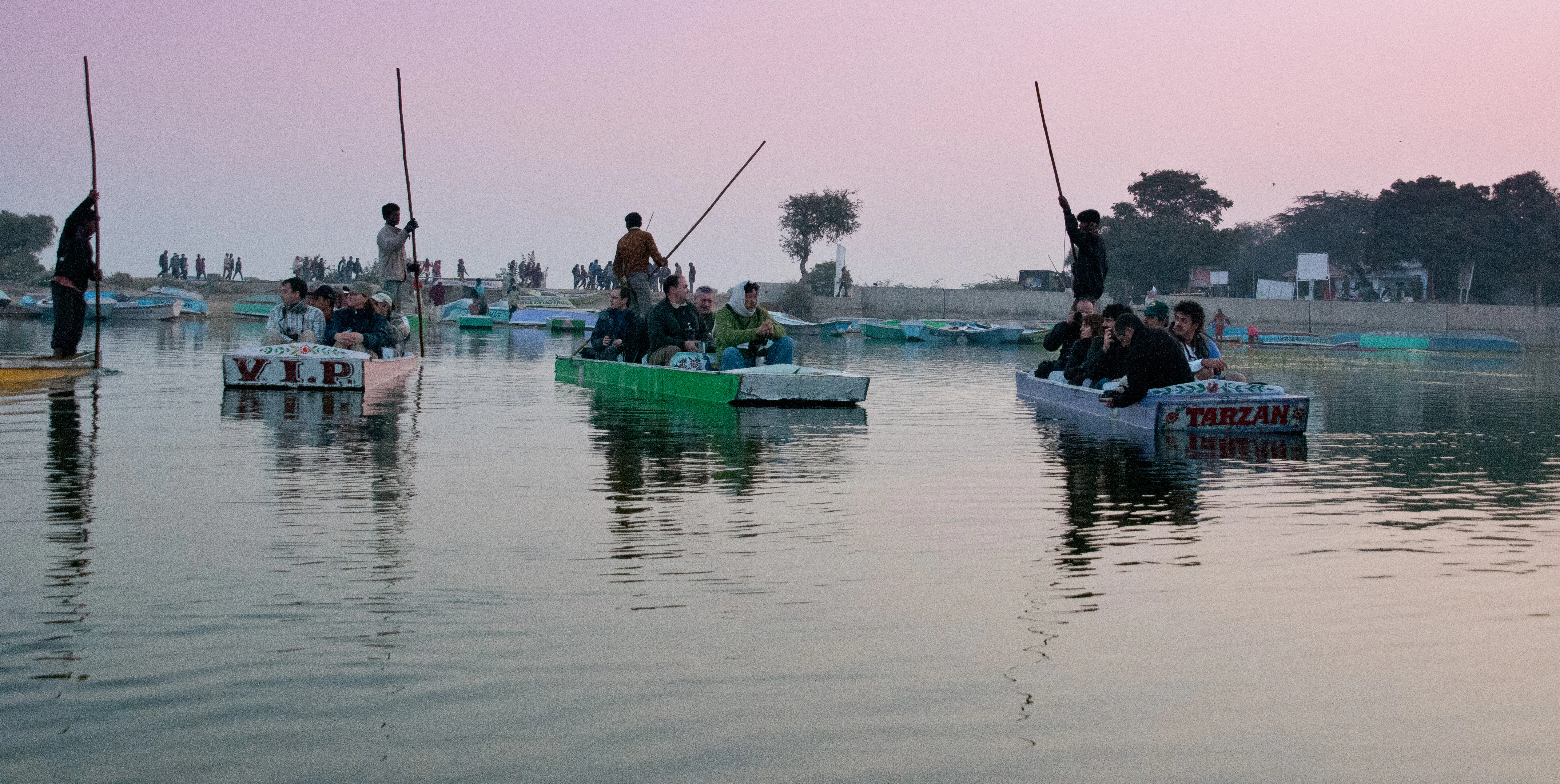 Several small flat-bottomed boats carrying passengers are being poled through calm water at sunrise.