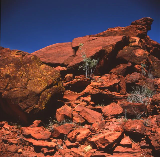 A close-up view of red sandstone rock formations and boulders under a clear deep blue sky in an arid Australian landscape.