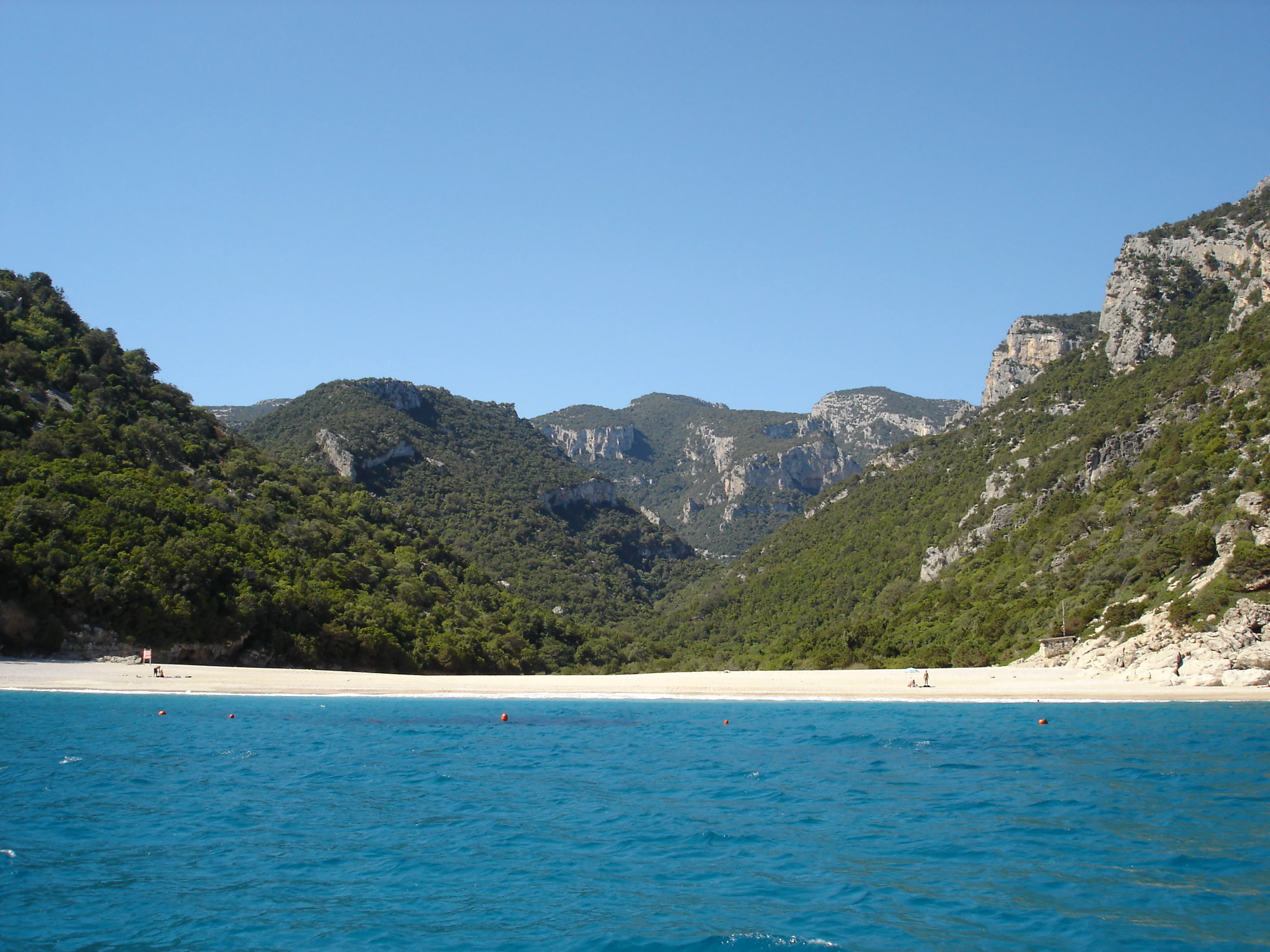 Blue water and sandy beach surrounded by lush green mountains under clear sky