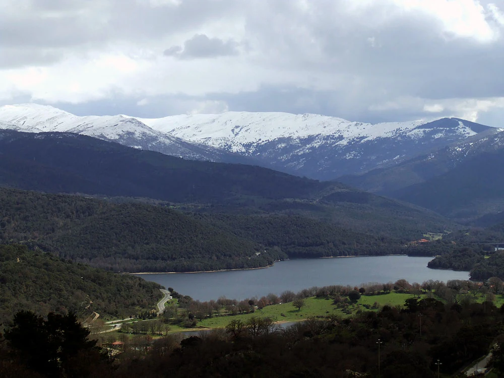 Snow-covered mountains overlook Gusana Lake in a winter landscape with forested hills and open fields