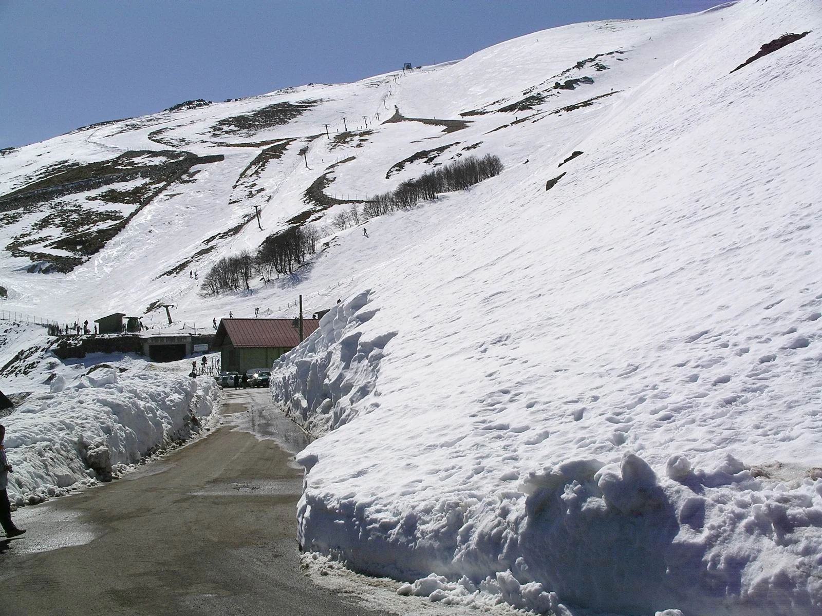 Snowy mountain slope with ski trails, a road, and a building with a red roof