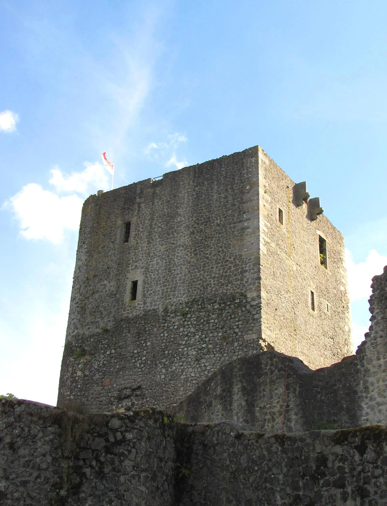 A low angle shot of the weathered stone ruins of a castle tower, specifically the East Palas of Weidelsburg, with a small flag flying at the top against a blue sky.