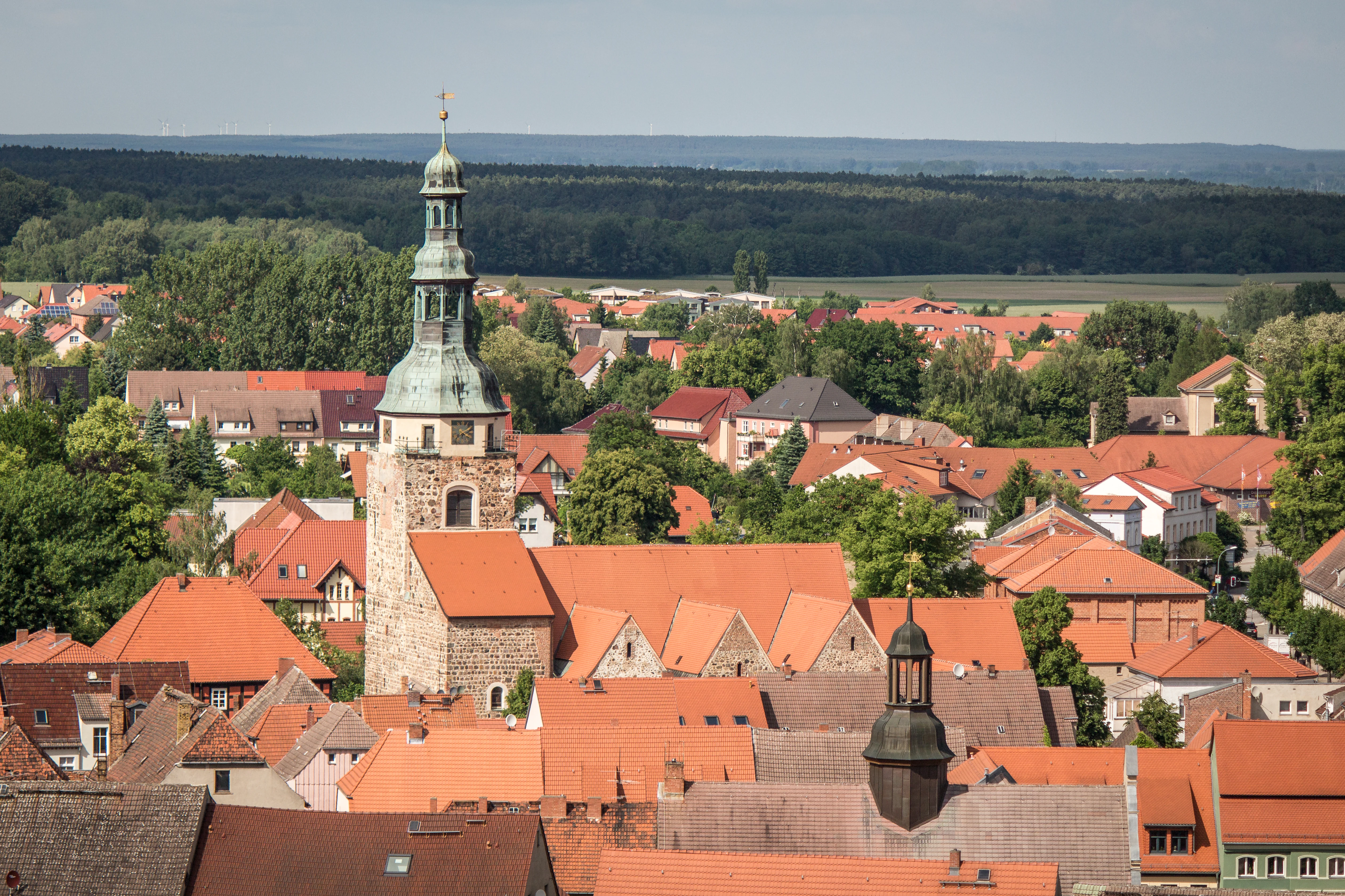 High angle view of a German town with red tiled roofs and a prominent church tower, with forested rolling hills in the background.