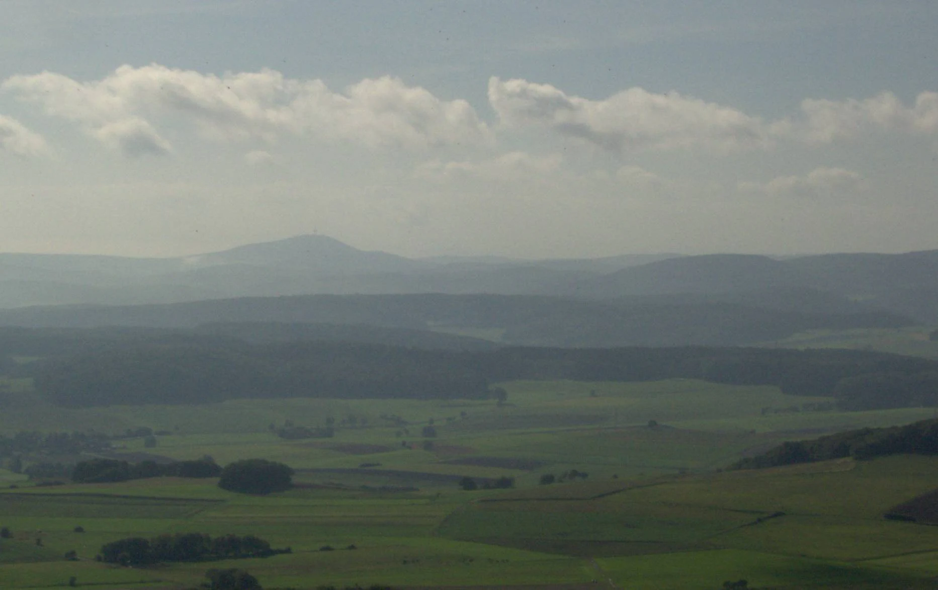 A wide, hazy landscape view of layered rolling hills and fields under a cloudy sky in Germany.