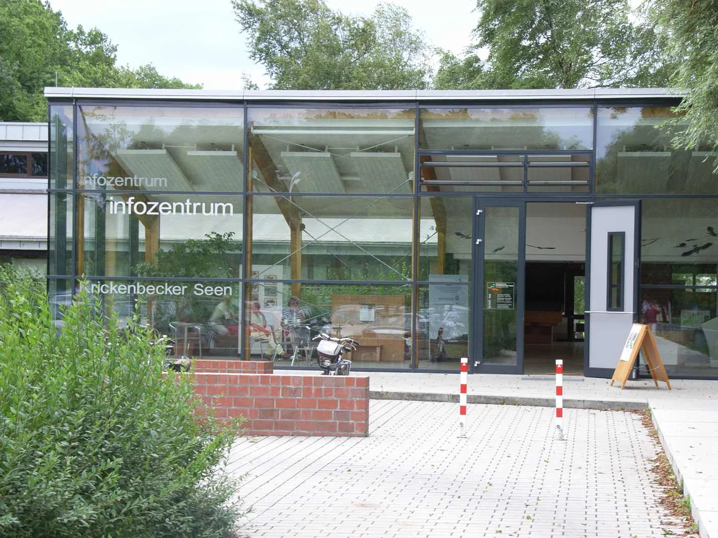 Modern glass-fronted visitor information center building with white text on windows and a red brick wall in the foreground.