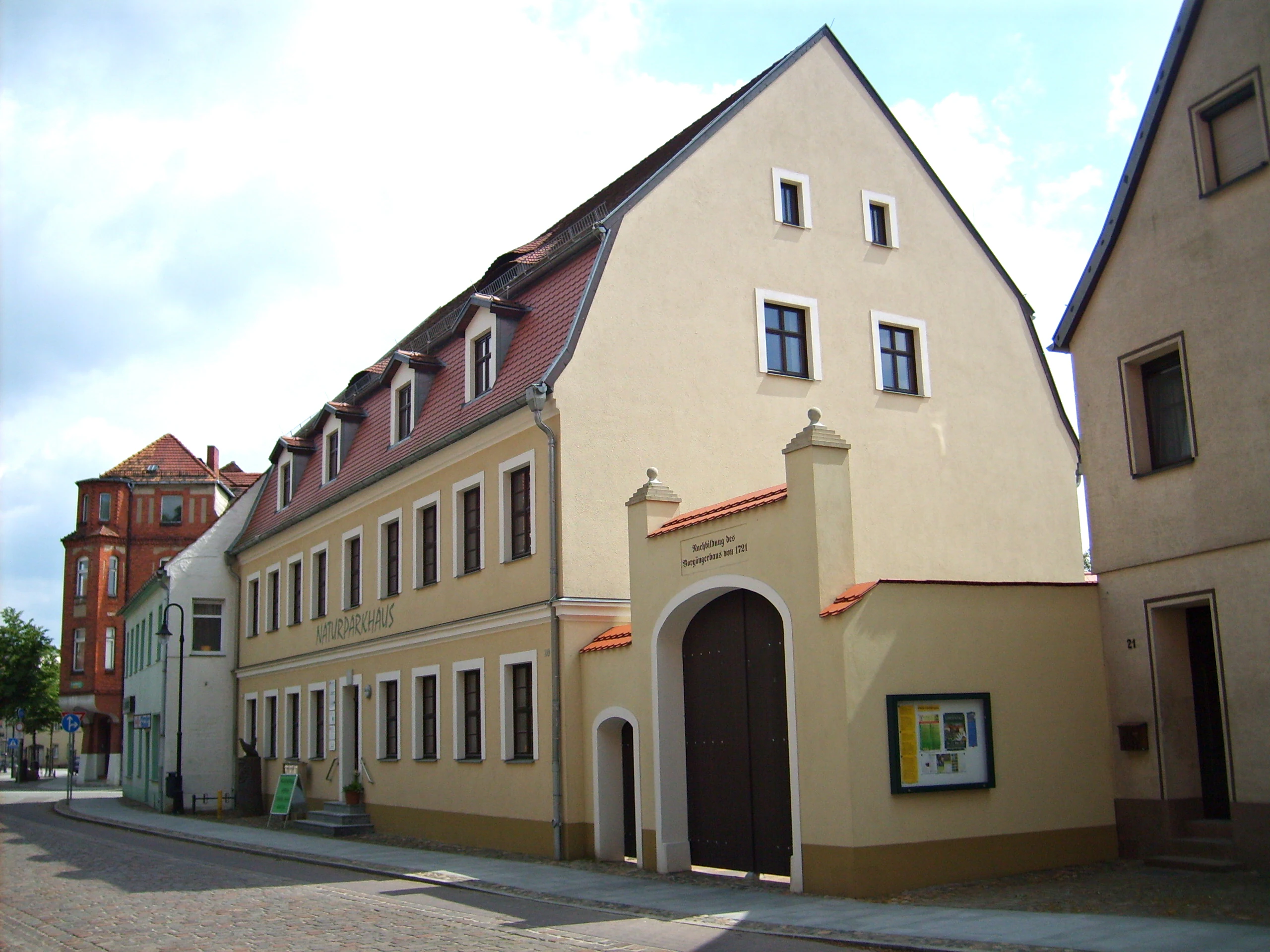 A multi-story tan building with a red tile roof and a gated entrance on a paved street in Bad Liebenwerda, serving as a park visitor center.