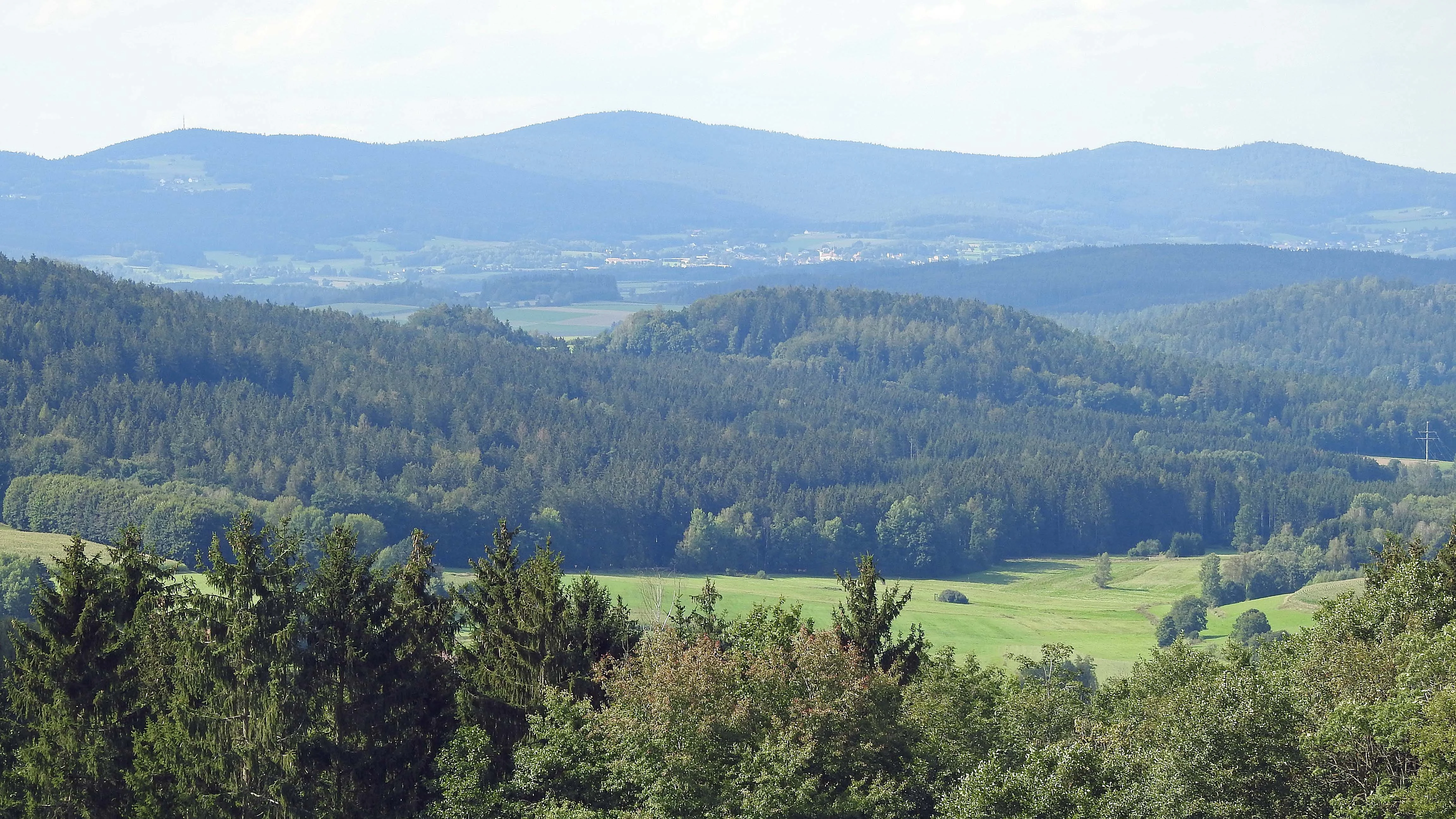 A wide, hazy panoramic view of forest-covered rolling hills and valleys in the Bavarian countryside.