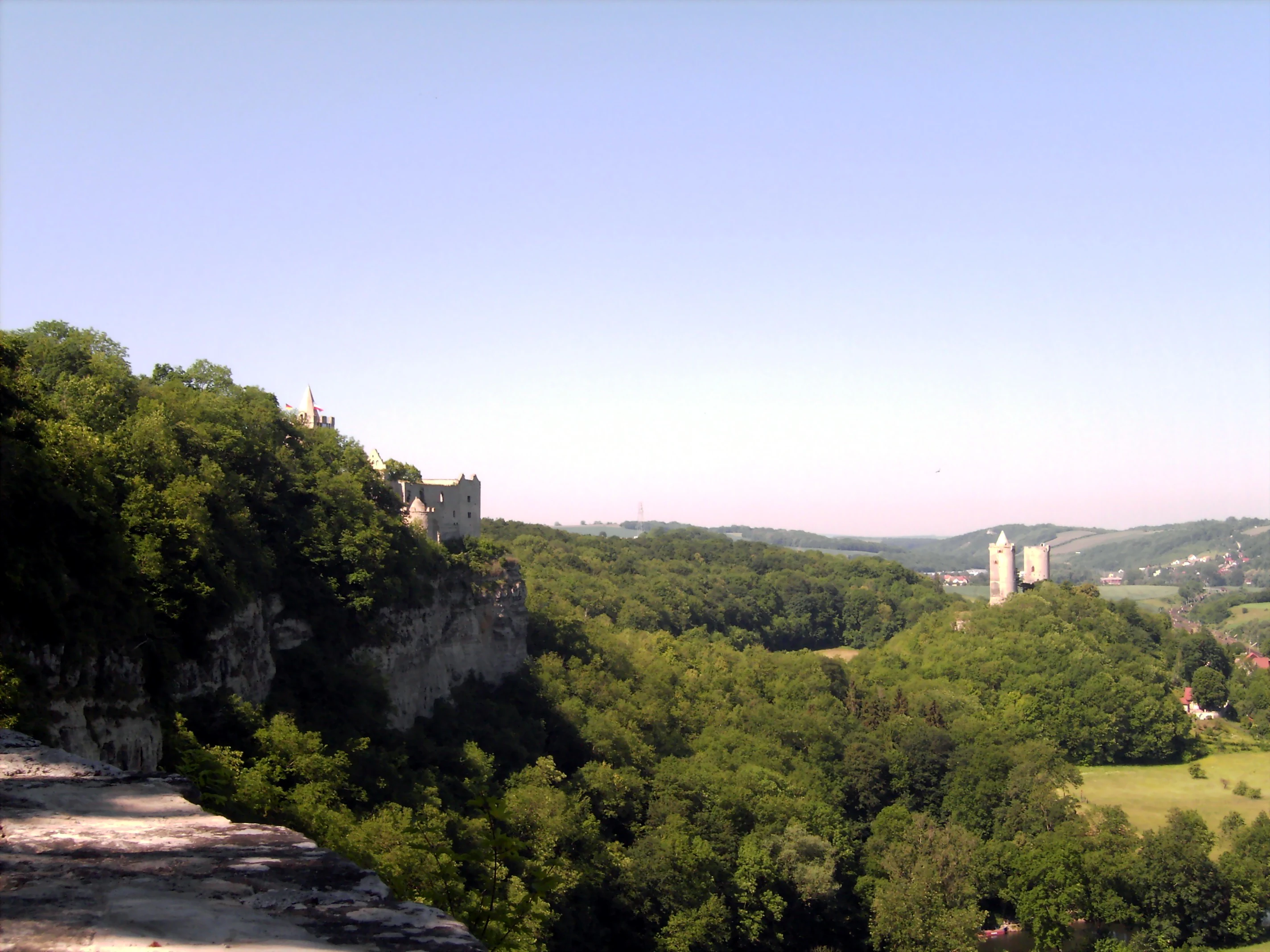 Wide landscape view featuring two historic stone castles perched on forested hillsides with a valley in between.
