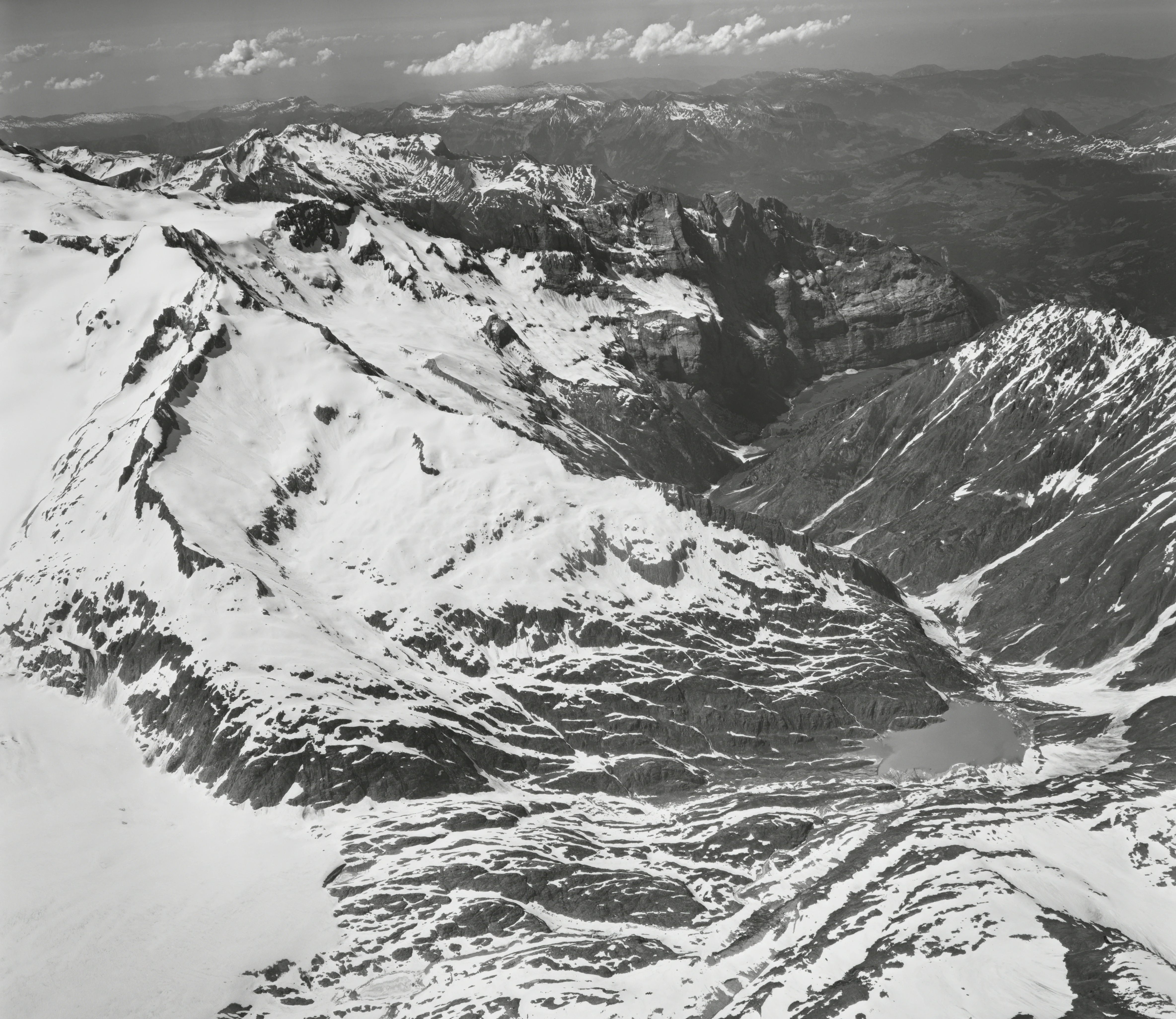 A black and white aerial photograph showing the Gauligletscher glacier flowing into the Urbachtal valley, surrounded by jagged snow-covered mountains.