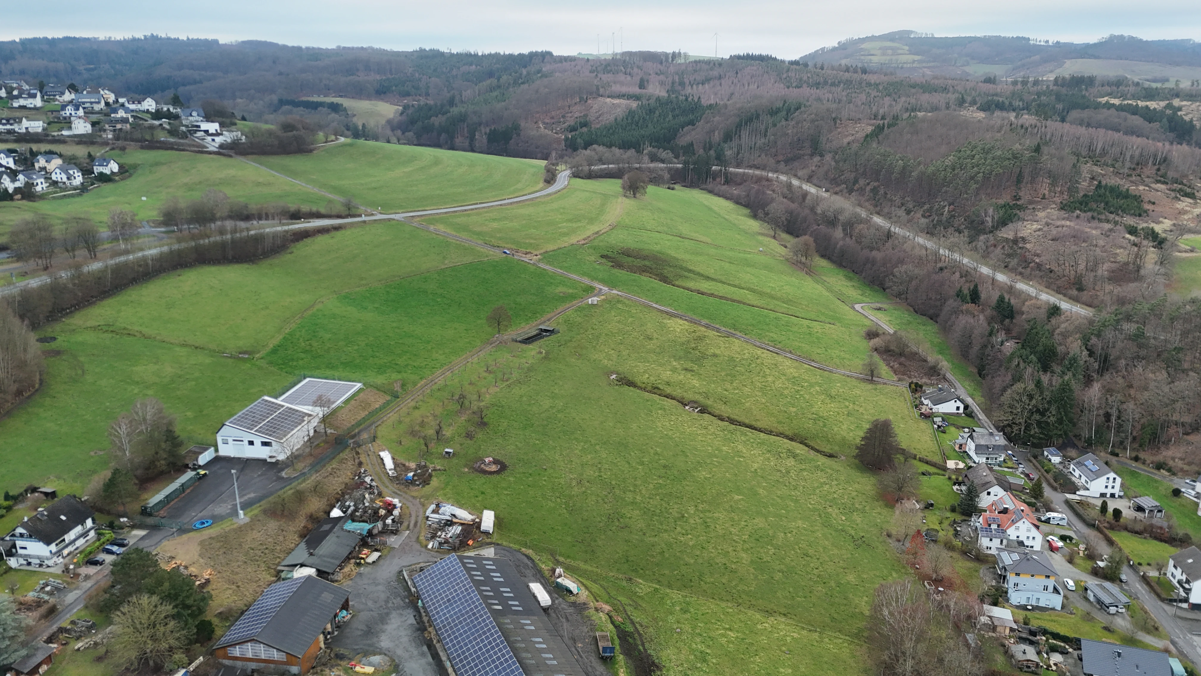 An aerial view of green rolling hills and meadows in Germany, with small residential clusters and forest edges visible.