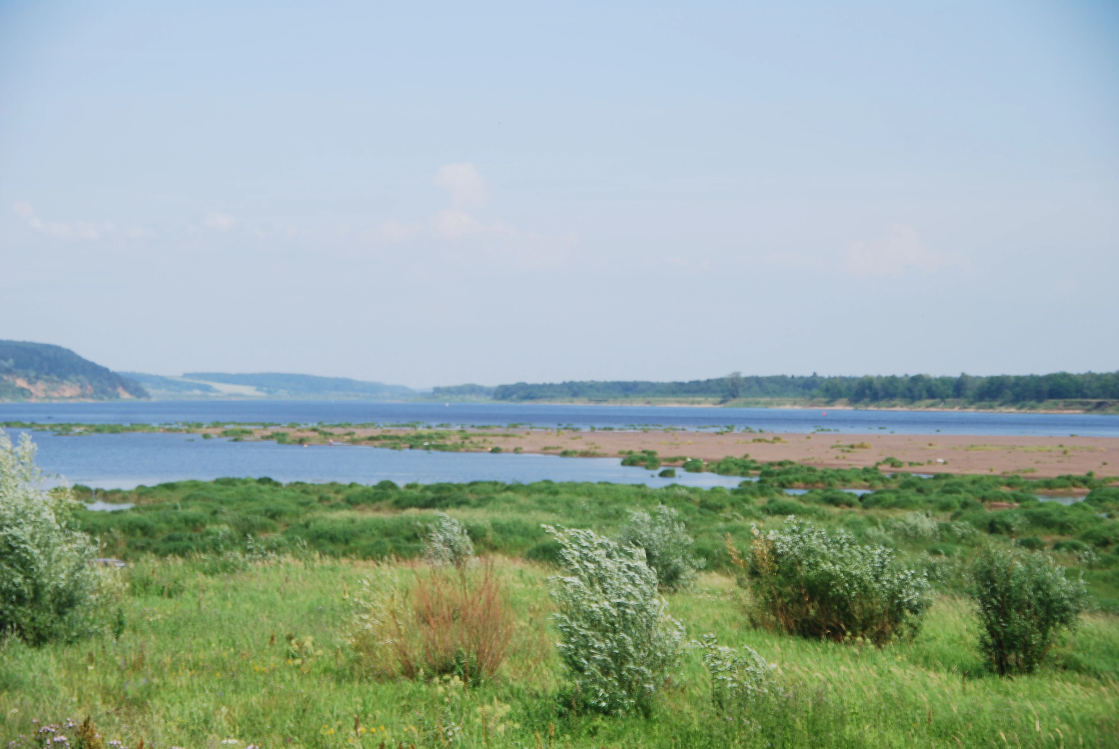 Wide landscape view of Kama River with green vegetation and distant hills under clear sky