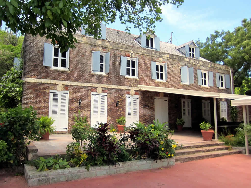 Exterior view of a three-story brick historic building with white window shutters and potted plants on a stone patio.