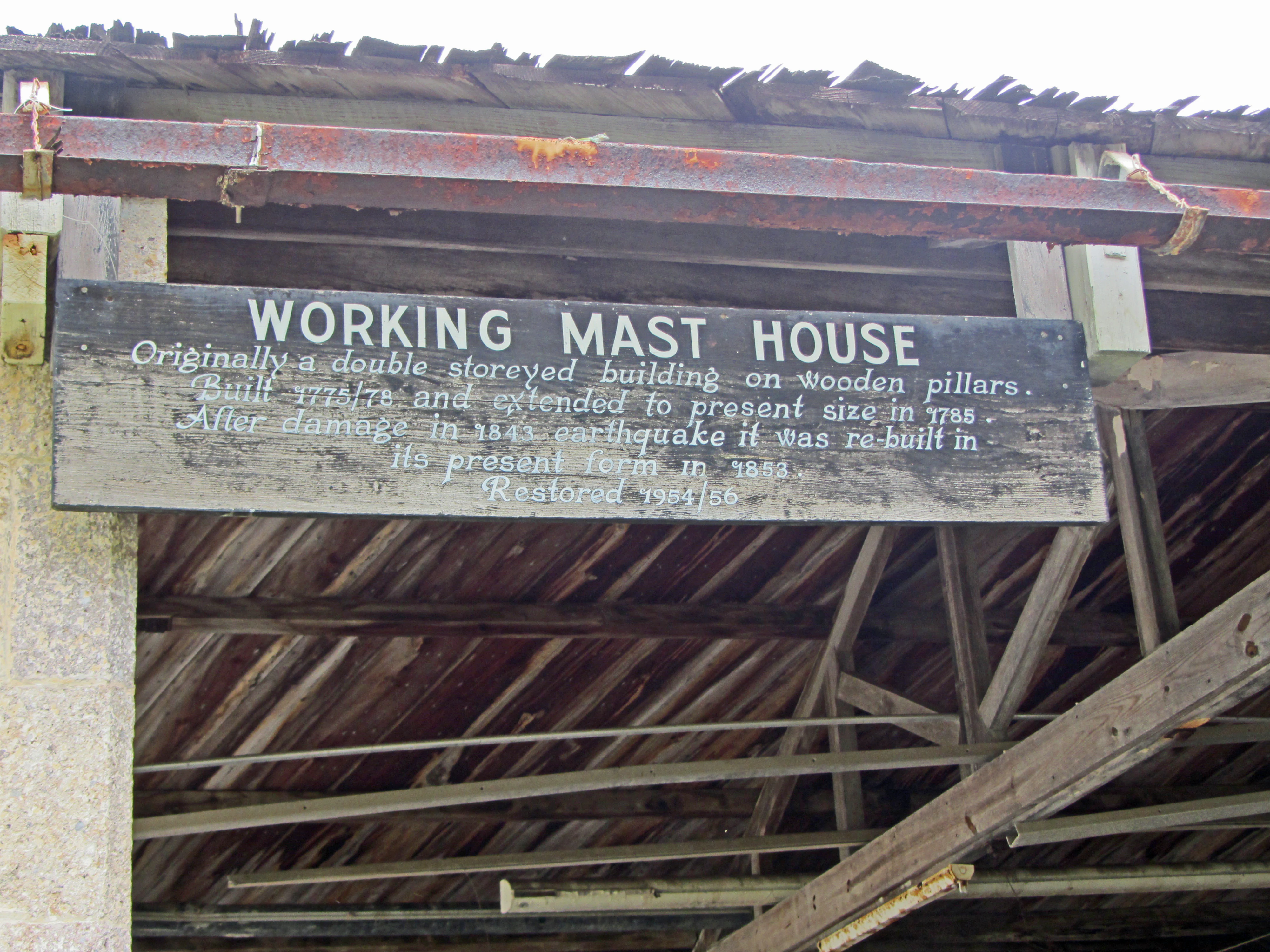 A wooden informational sign mounted on a historic structure reads Working Mast House, followed by historical text about the building's construction and restoration.