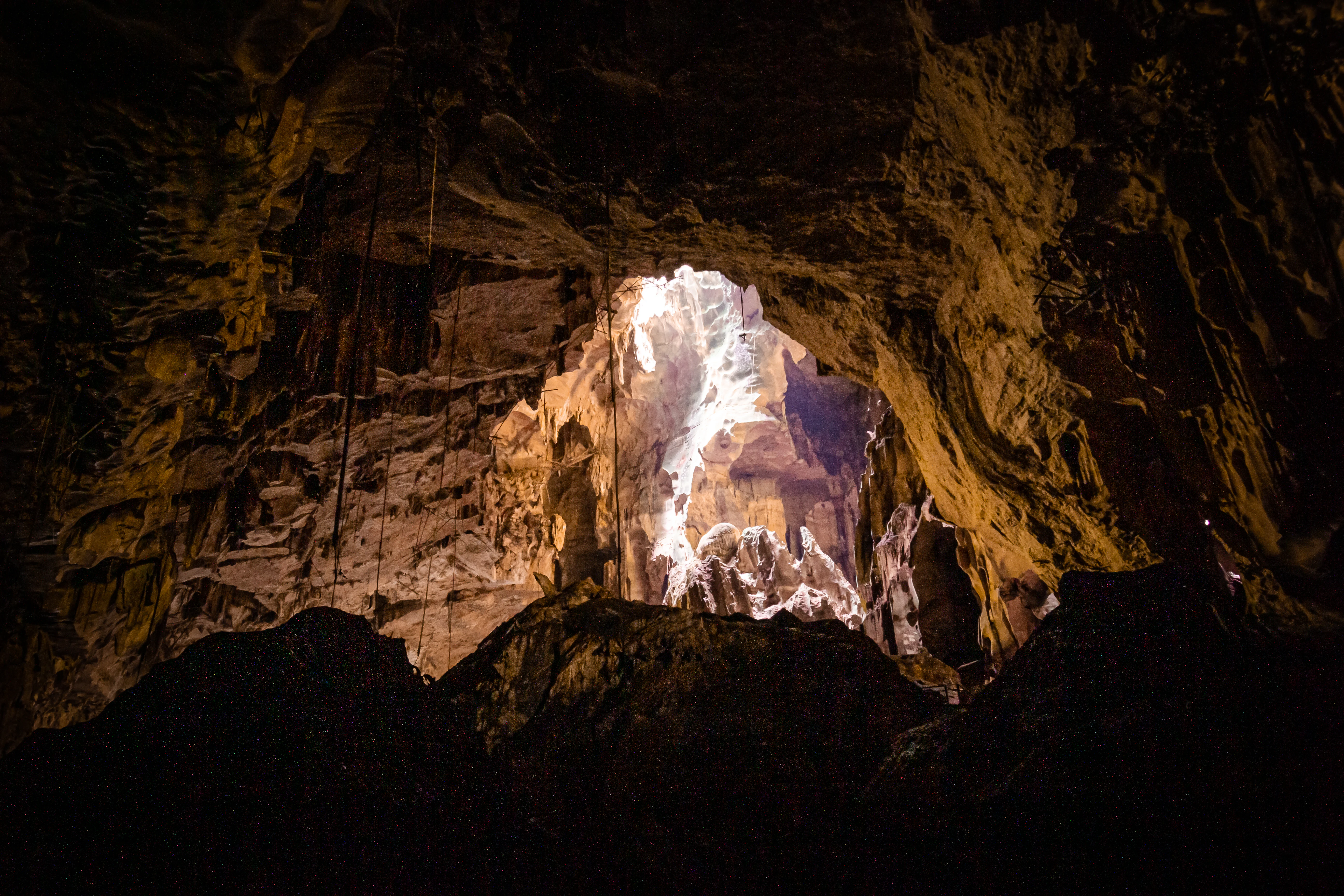 Dark cave interior with rocky walls and a bright opening revealing daylight outside
