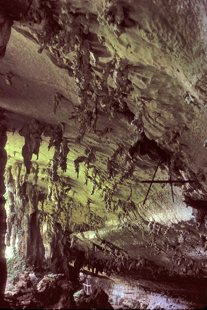 Stalactites hanging from the cave ceiling with rocky formations in the background