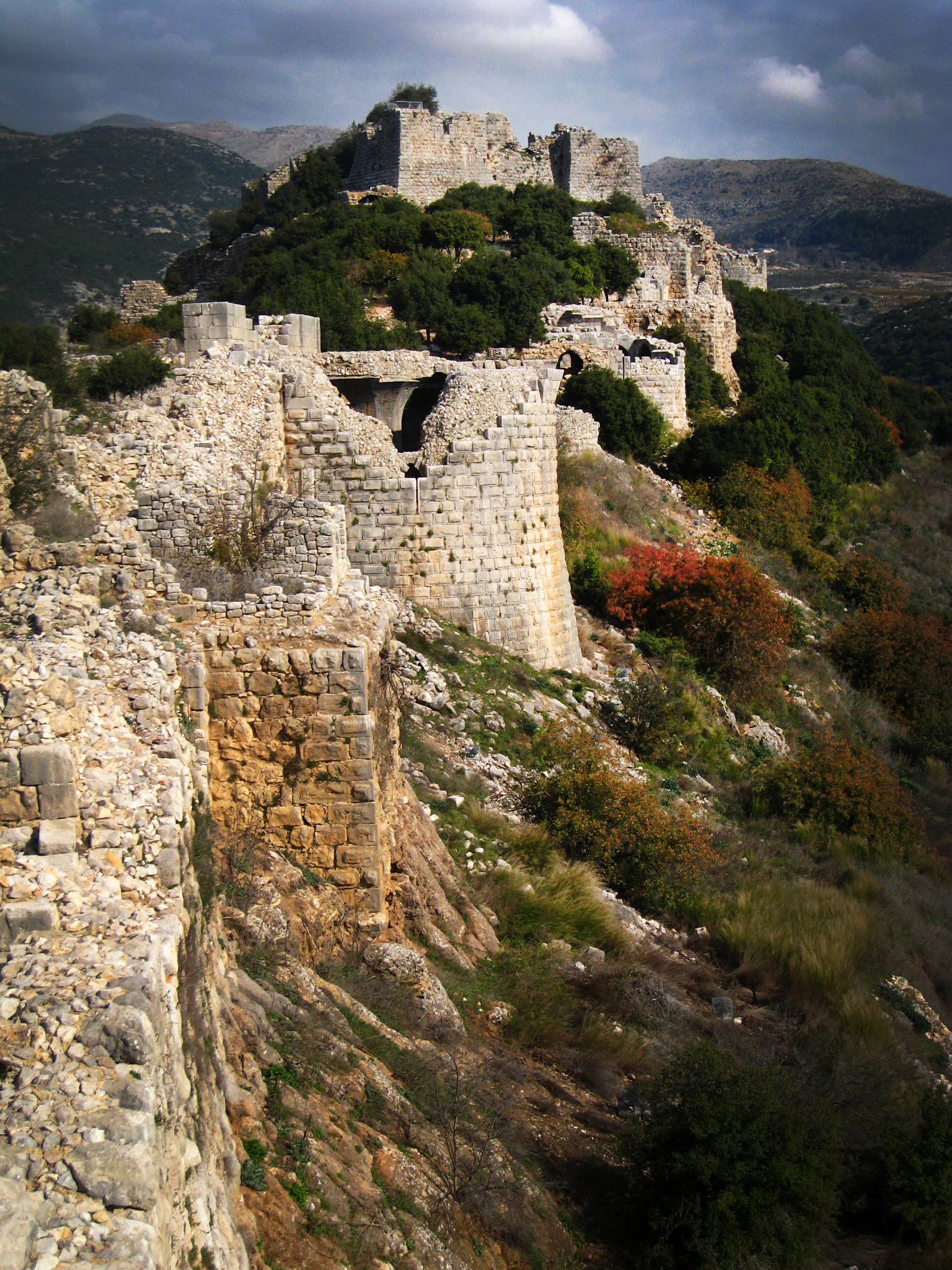 Stone walls and towers of Nimrod Fortress on a rocky hillside with vegetation and mountains in the background