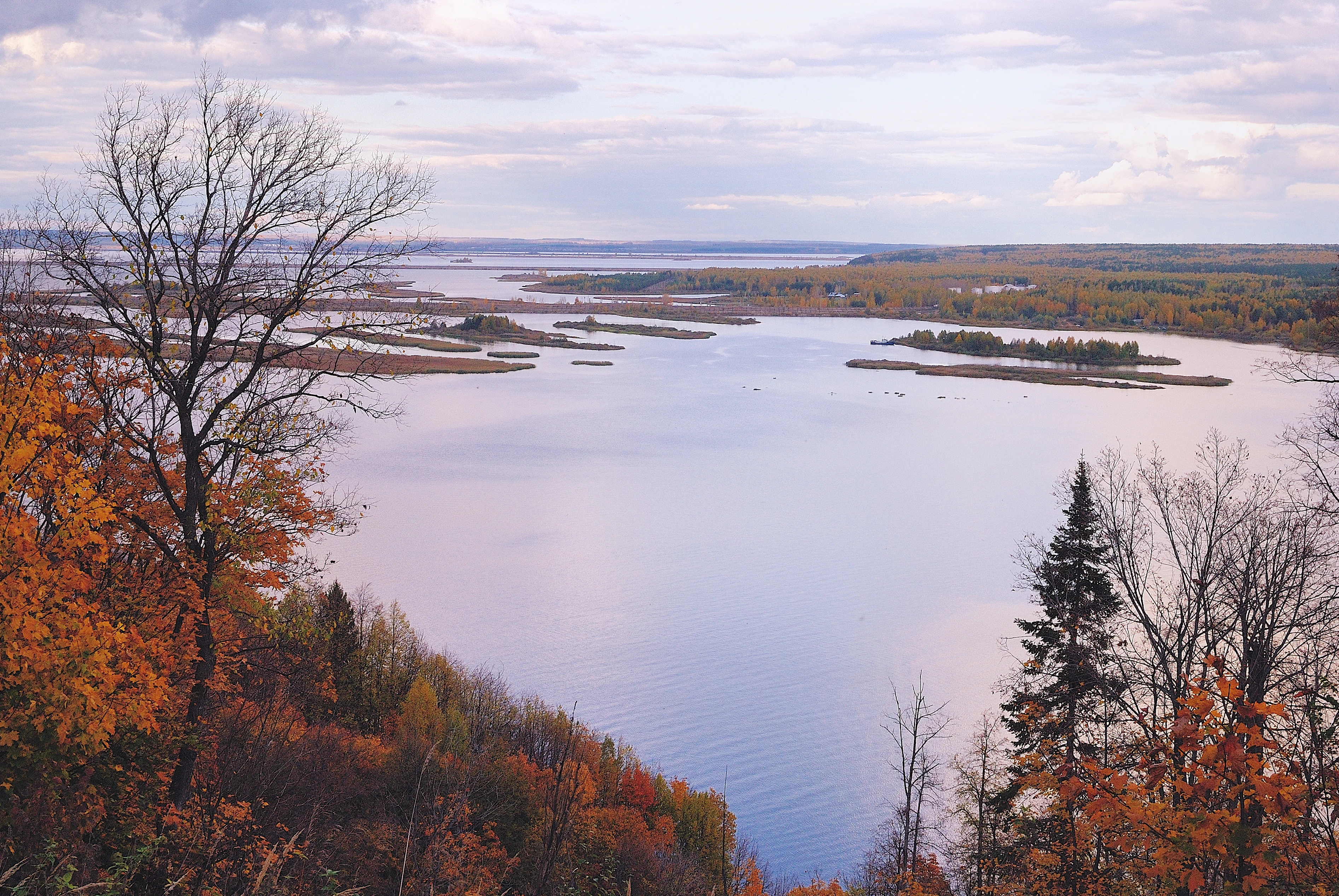 Wide view of the Kama River with autumn-colored trees along the shore and several small islands in the water