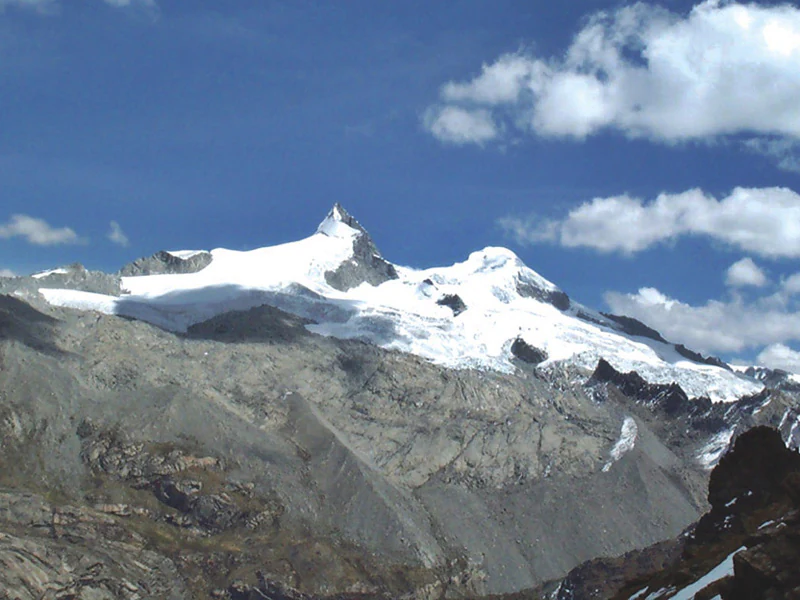 Una vista amplia de la cordillera nevada de Nevado Pariacaca bajo un cielo azul con nubes dispersas.