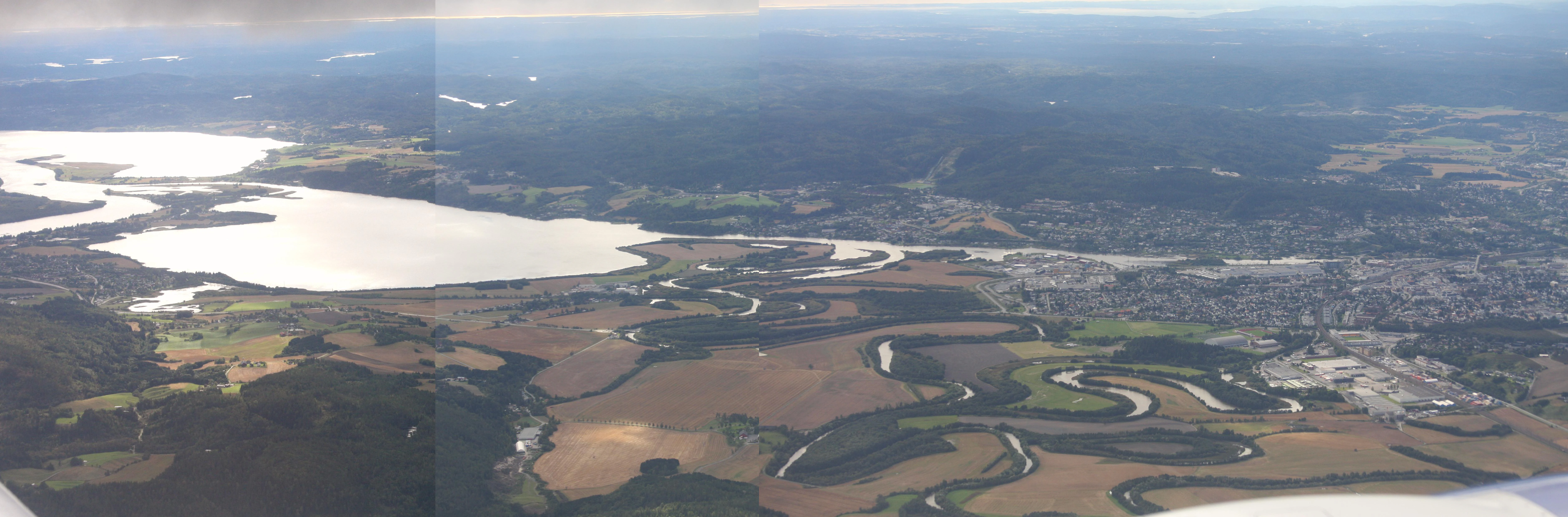 Wide aerial photograph showing lakes, wetlands, agricultural fields, forests, and a town in the Nordre Øyeren Nature Reserve area.