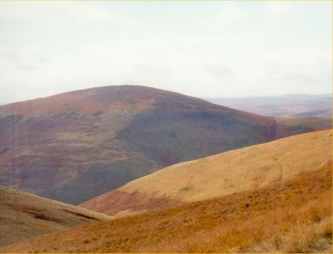 Rolling hills and valley landscape with brown and green terrain under a partly cloudy sky