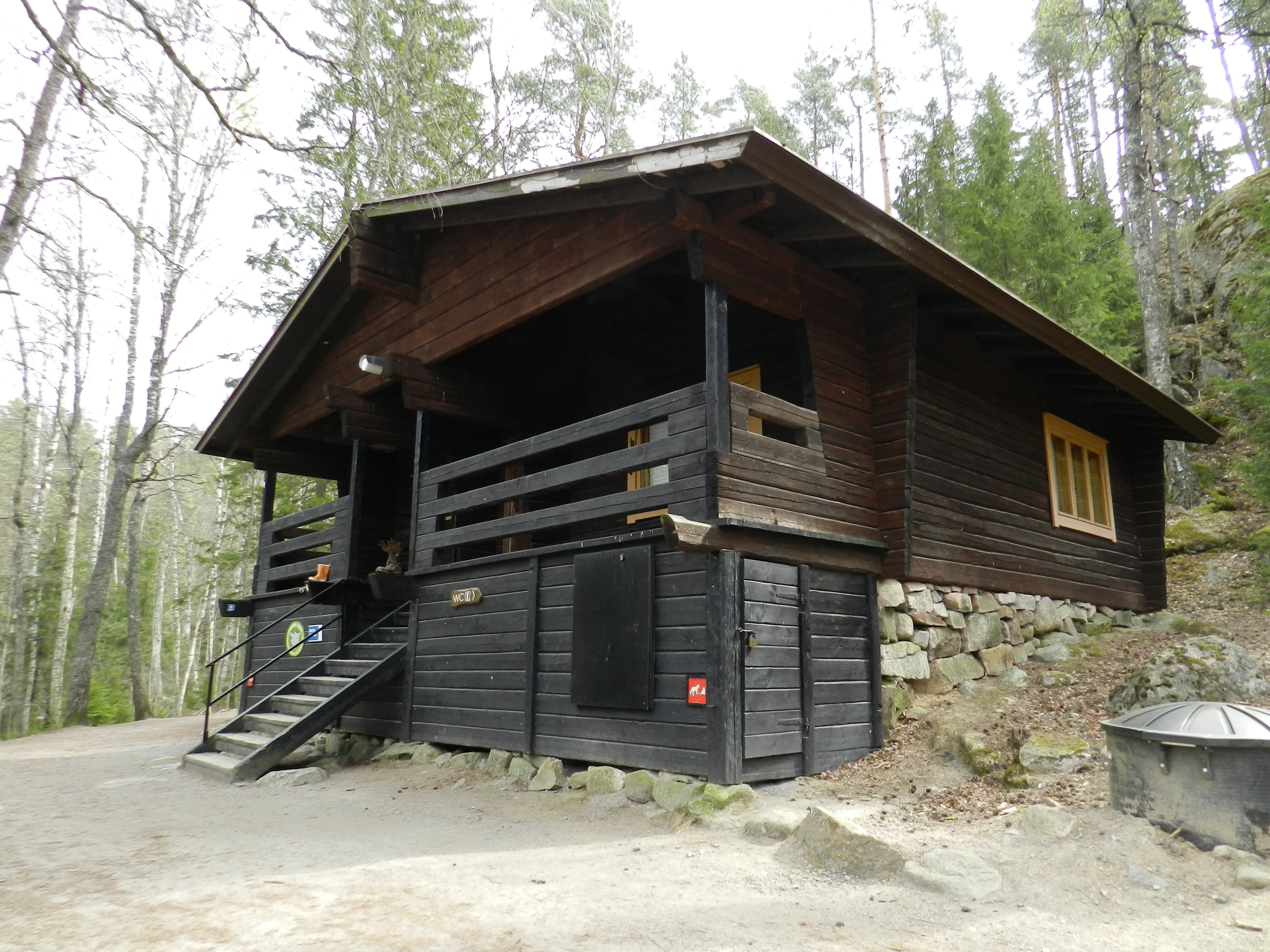 Wooden guide hut with stone foundation and staircase, surrounded by forest, located in Nuuksio National Park