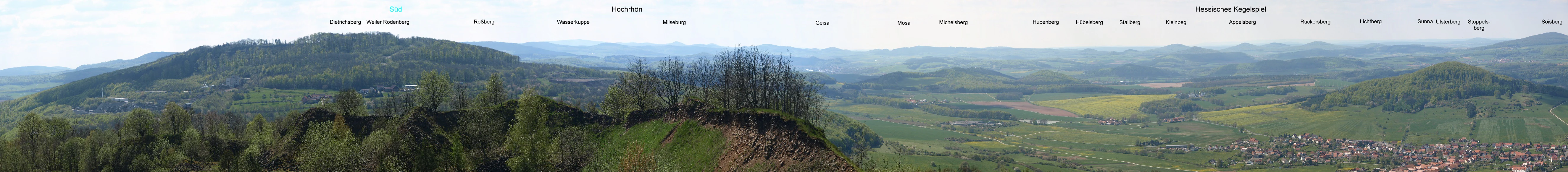 Panoramic landscape view from a high vantage point overlooking rolling forested hills, valleys, and distant mountains under a cloudy sky.