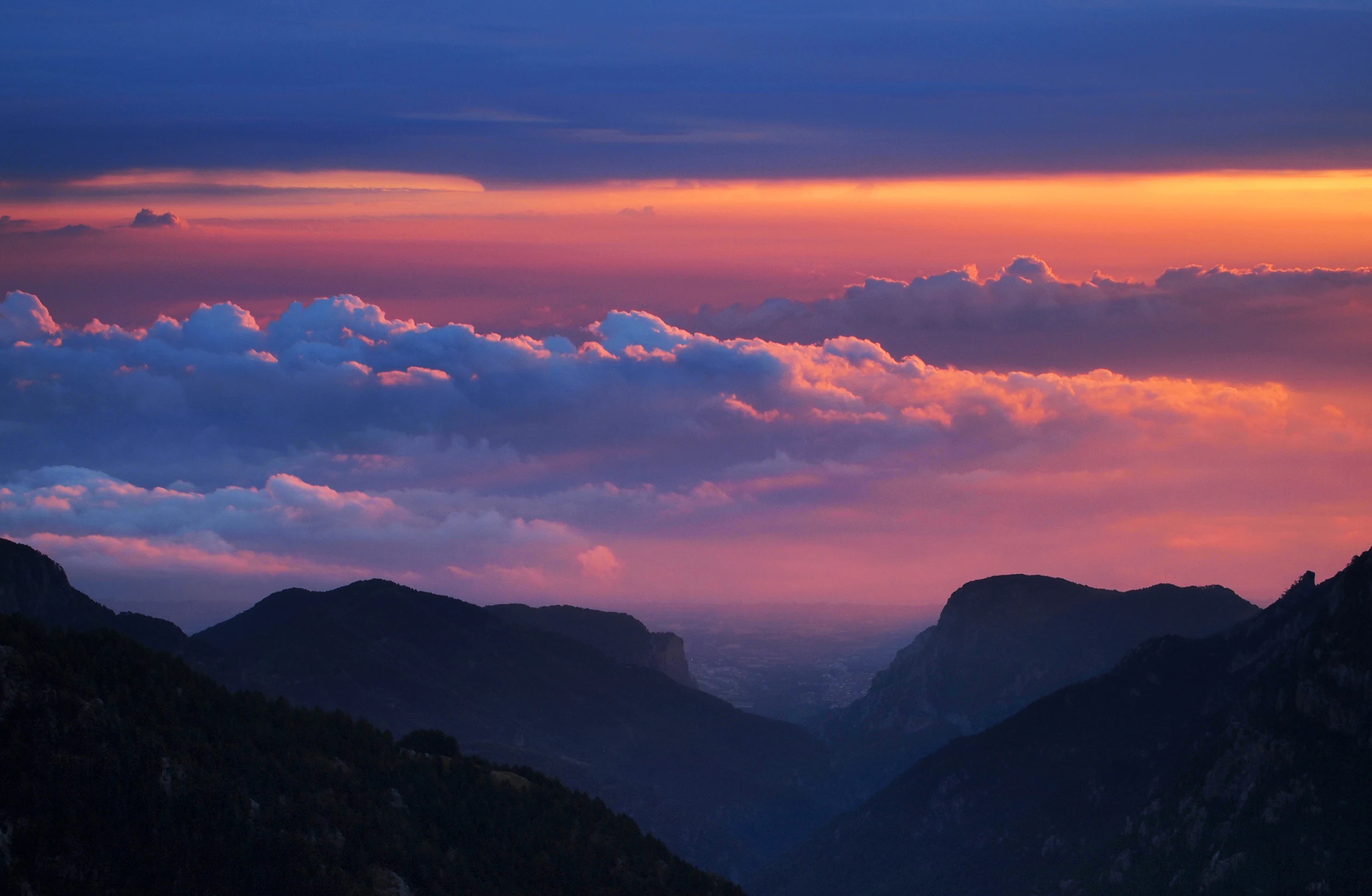 Dramatic sunset over silhouetted mountain ridges with purple and orange clouds filling the sky.