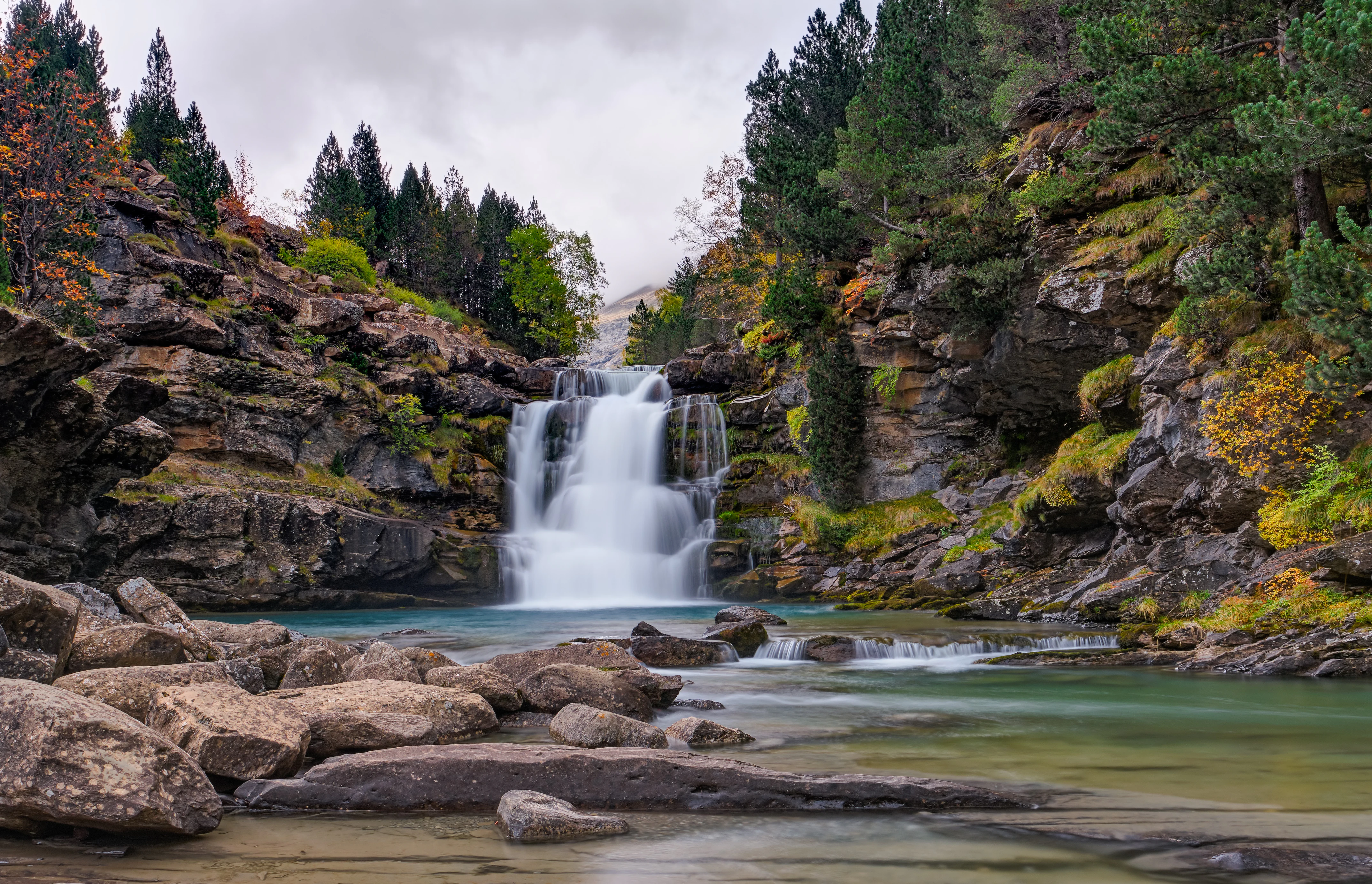 Waterfall with rapids flowing over rocks in a mountainous valley surrounded by forested cliffs