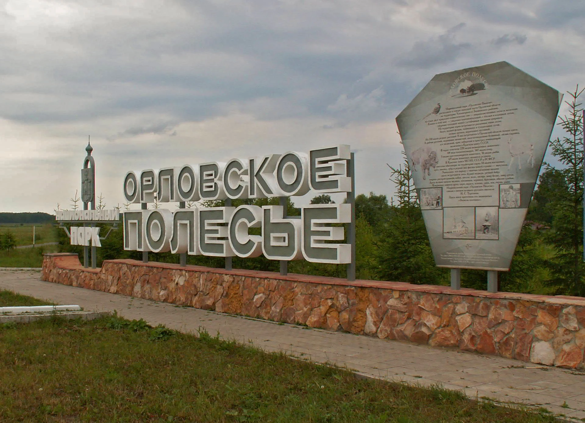 A large, stone-based sign with raised white lettering in Cyrillic reading Orlovskoye Polesye stands at the park entrance, accompanied by an informational plaque on the right.