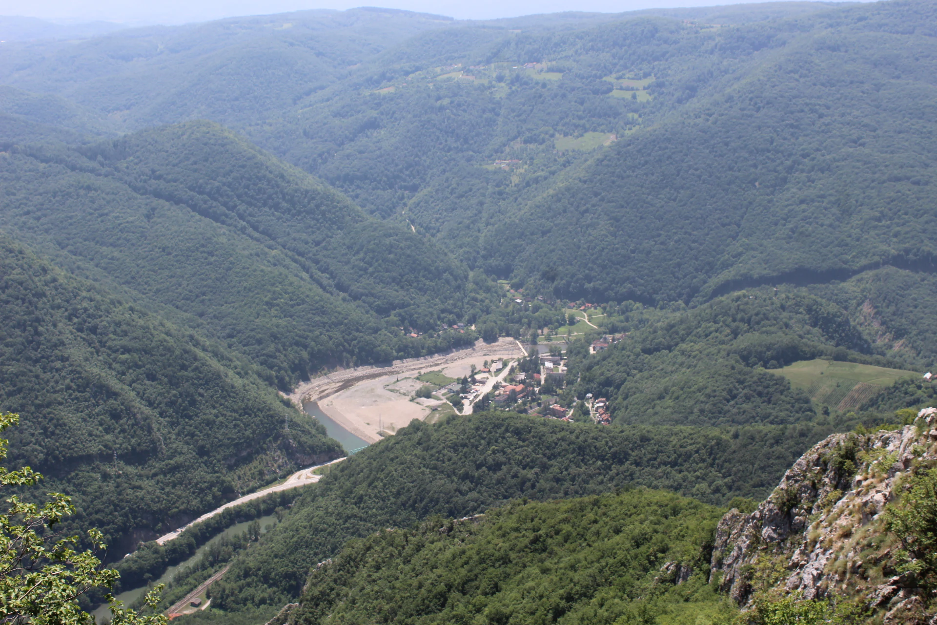 Wide landscape of a river valley surrounded by forested hills and mountains