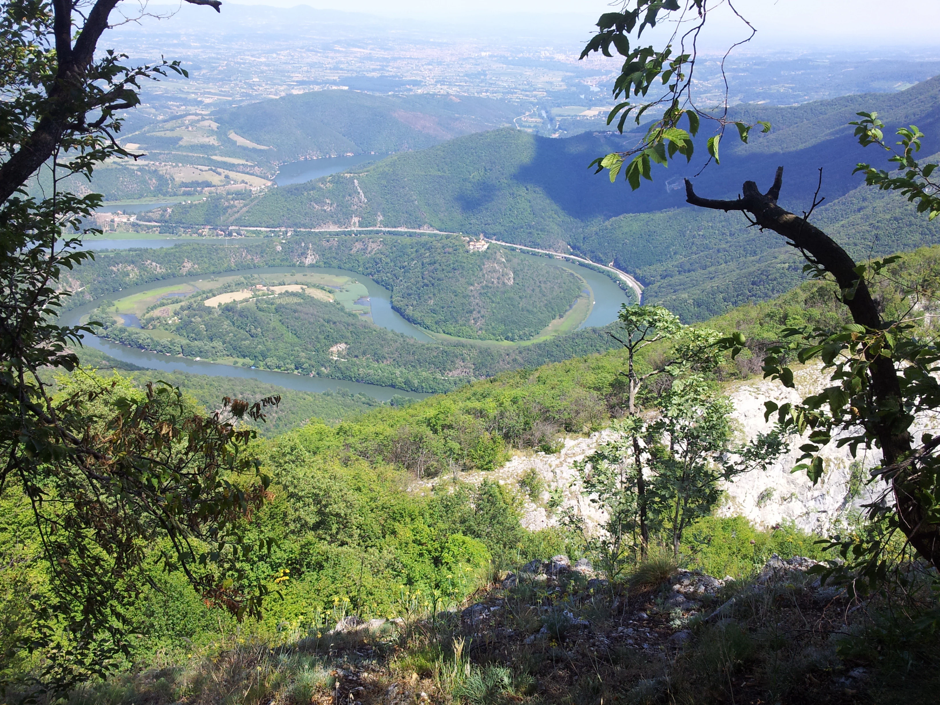 A river meandering through a valley surrounded by green hills and forests with distant plains visible