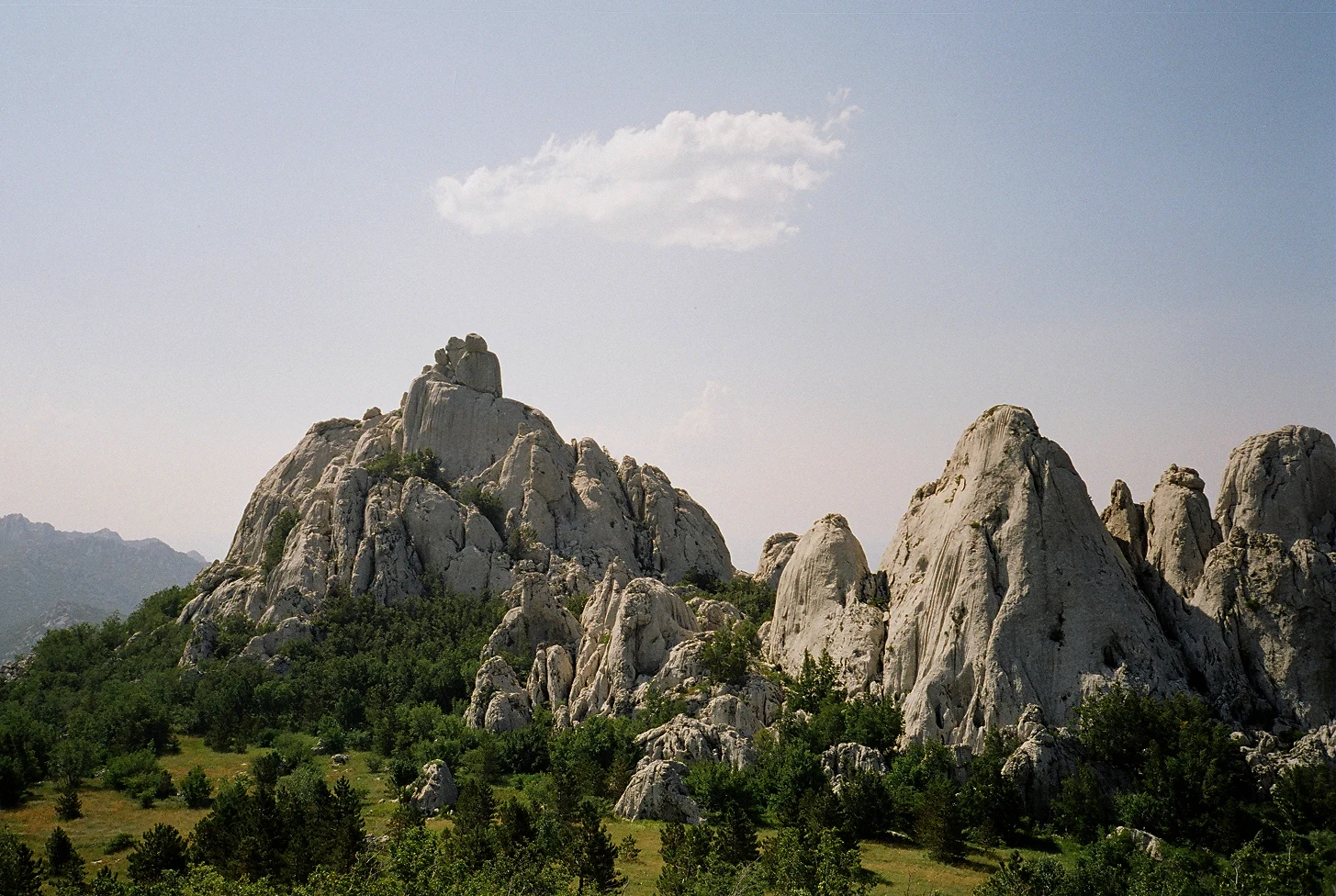 Mountainous landscape with rocky limestone formations and green vegetation under clear sky