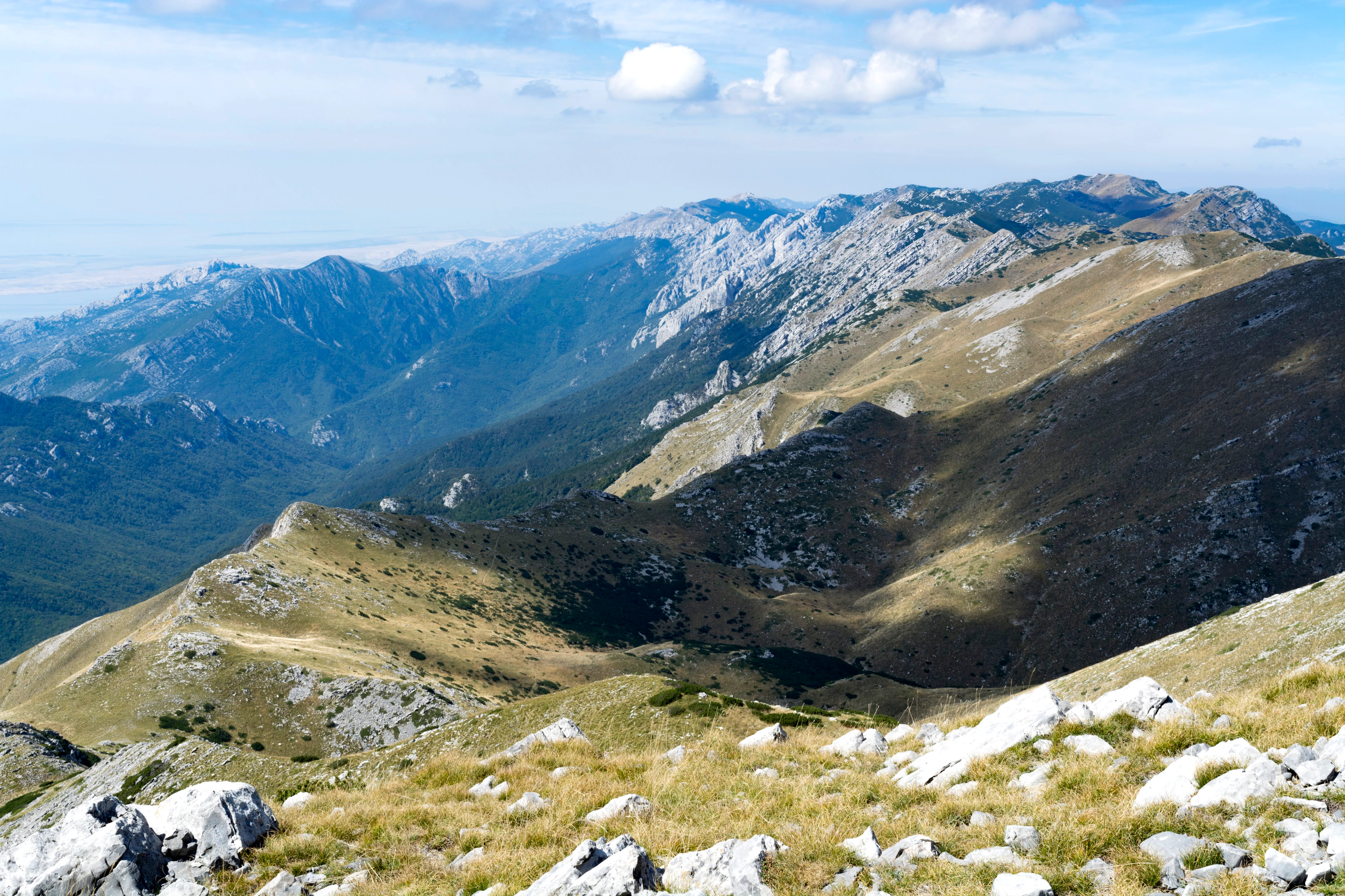 Rocky mountain peaks, grassy slopes, and distant mountain ranges under a partly cloudy sky